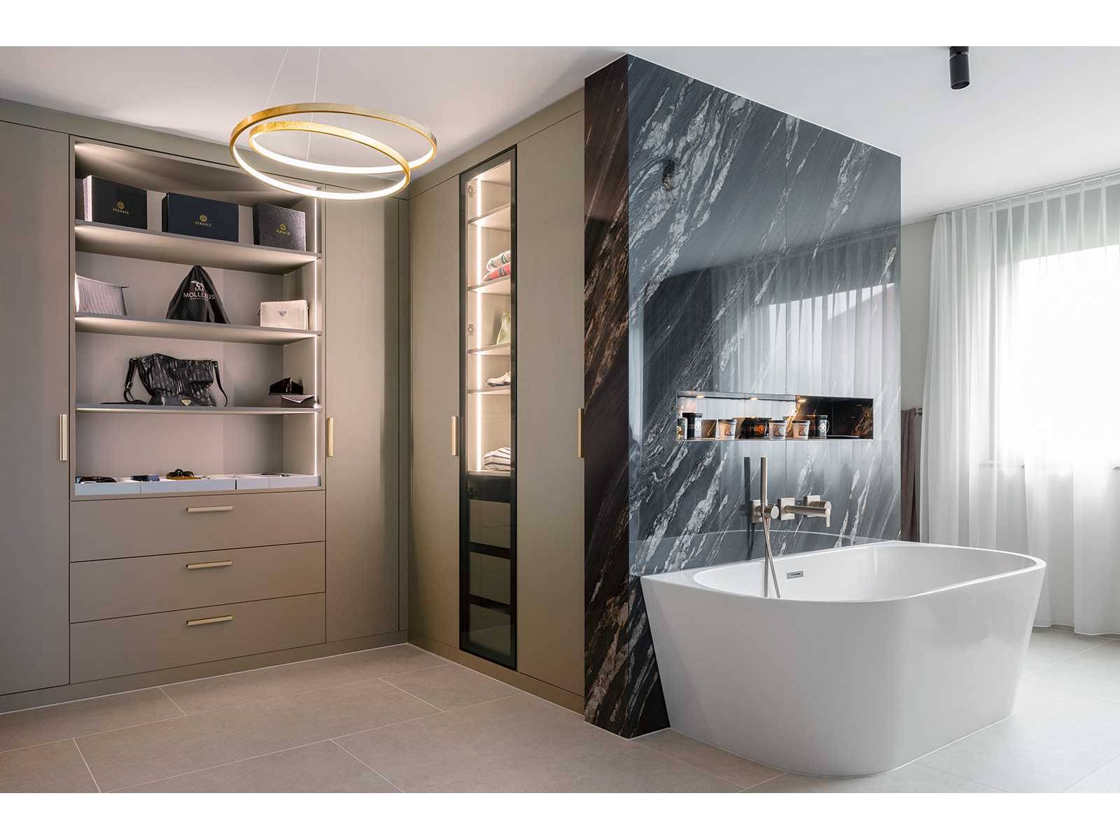 Vor einer Wand in dunkler Marmoroptik steht die freistehende Wanne, der angrenzende Ankleidebereich greift Materialität und Farbigkeit auf. Die Manufaktur aus der Ostschweiz plante den individuell abgestimmten Innenausbau. ELBAU.