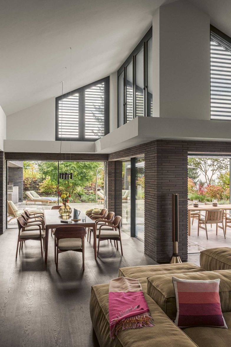 Bodentiefe Schiebefenster von Swiss Fine Line verbinden den Wohn- und Essbereich mit der Terrasse. Die geschwungenen Linien der Nussbaumstühle sind ein gelungener Kontrast zu der geradlinigen Architektur.