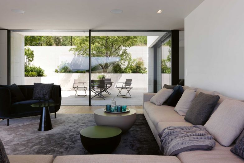 Der Innenhof ermöglicht trotz der Hanglage eine offen gestaltete Rückseite mit grosszügiger, bodentiefer Verglasung. Er erweitert den Wohnraum und bietet einen Schattenplatz an heissen Sommertagen. Die Sitzlandschaft ist von Minotti; der Zweisitzer «Vuelta» von Jaime Hayon für Wittmann.