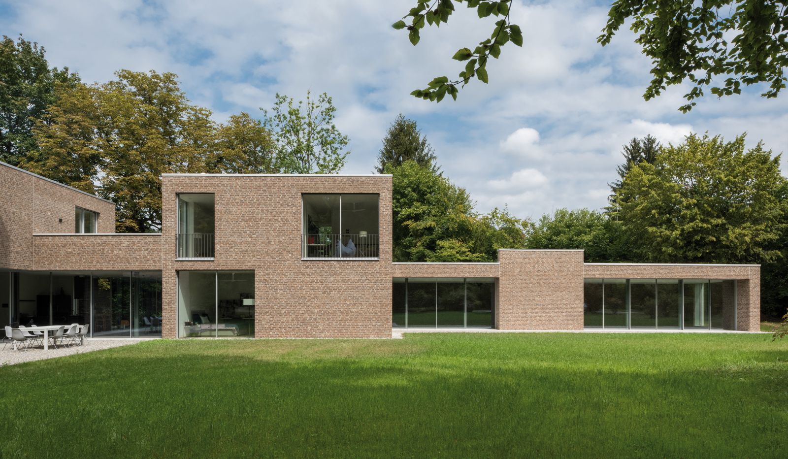 Das Volumen aus stufenförmig versetzten und ineinandergreifenden Kuben mit Fassaden aus Backstein und Glas steht bei der Drei-Generationen-Villa in einem harmonischen Dialog zur grosszügigen Parklandschaft im Süden.