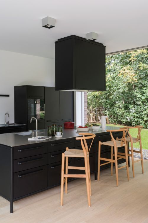 Die maskuline Küche der innovativen ­Designmarke Vipp begeistert die Hausbewohner dank ihrer ­hohen Funktionalität. Arbeitsflächen aus Chromstahl, Deckenleuchten «Compass Box» von Flos, Barstühle von Cultfurniture.