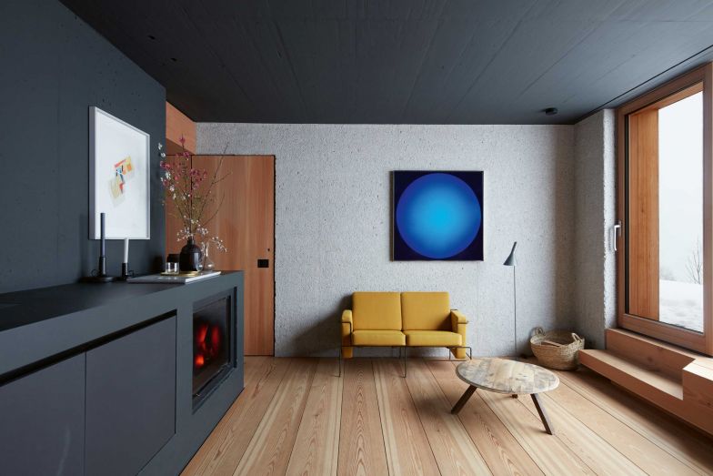 In der Gästesuite im dritten Geschoss gibt es eine Wand aus Beton, die ein Teil des Fundaments ist. Petri liess sie sandstrahlen, um ihr eine abwechslungsreiche Textur zu verleihen. Die Treppe zur Aussenterrasse ist aus einem einzigen Stück Holz gefertigt. Der Beton des Kerns, in dem Schornstein und Aufzug untergebracht sind, wurde hier schwarz gestrichen. Zweisitziger Sessel «Traffic» von Konstantin Grcic für Magis.; Stehleuchte «AJ» von Arne Jacobsen für Louis Poulsen.