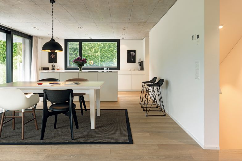 Das Herzstück des Erdgeschosses bilden die moderne, offene Küche und der Essbereich, der bei schönem Wetter gerne an den Sitzplatz im Garten verlegt wird. Küche von Meienberger und Egger AG, Barhocker «Carbonchair» von Moooi, Esstischstühle «Form» von Normann Copenhagen und «Slab» von Tom Dixon. 
