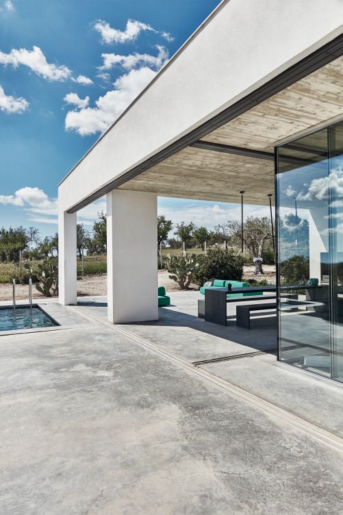 Die Glasschiebetüren führen ins Wohnzimmer. Einen halben Meter vor ihnen verlaufen die Schienen der Sonnenschutzpaneele. Die Decke wurde nicht verputzt, sondern in Sichtbeton belassen. 