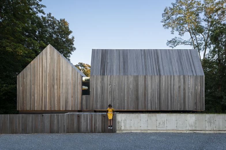 Ein Bollwerk aus Holz und Beton und die geschlossene Dachhaut schützen vor Einblicken und dem Strassenlärm. Vor den beiden rechtwinklig zueinanderstehenden Hausteilen erstreckt sich ein grosser Parkplatz.