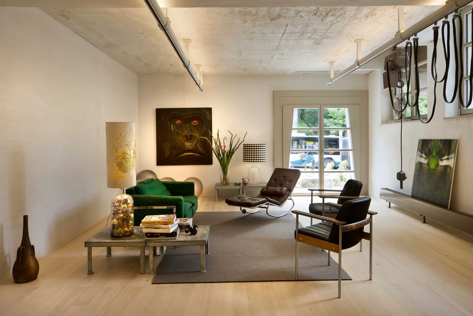 Das Wohnzimmer mit dem ehemaligen Laufkran (nun ein Lichtobjekt) des Steinmetzateliers und einem währschaften Boden aus massivem Tannenholz. Wohlkonstruierte Stillleben verraten die Leidenschaft der Bauherren für ausgefallene Leuchten, die sie selber fertigen.