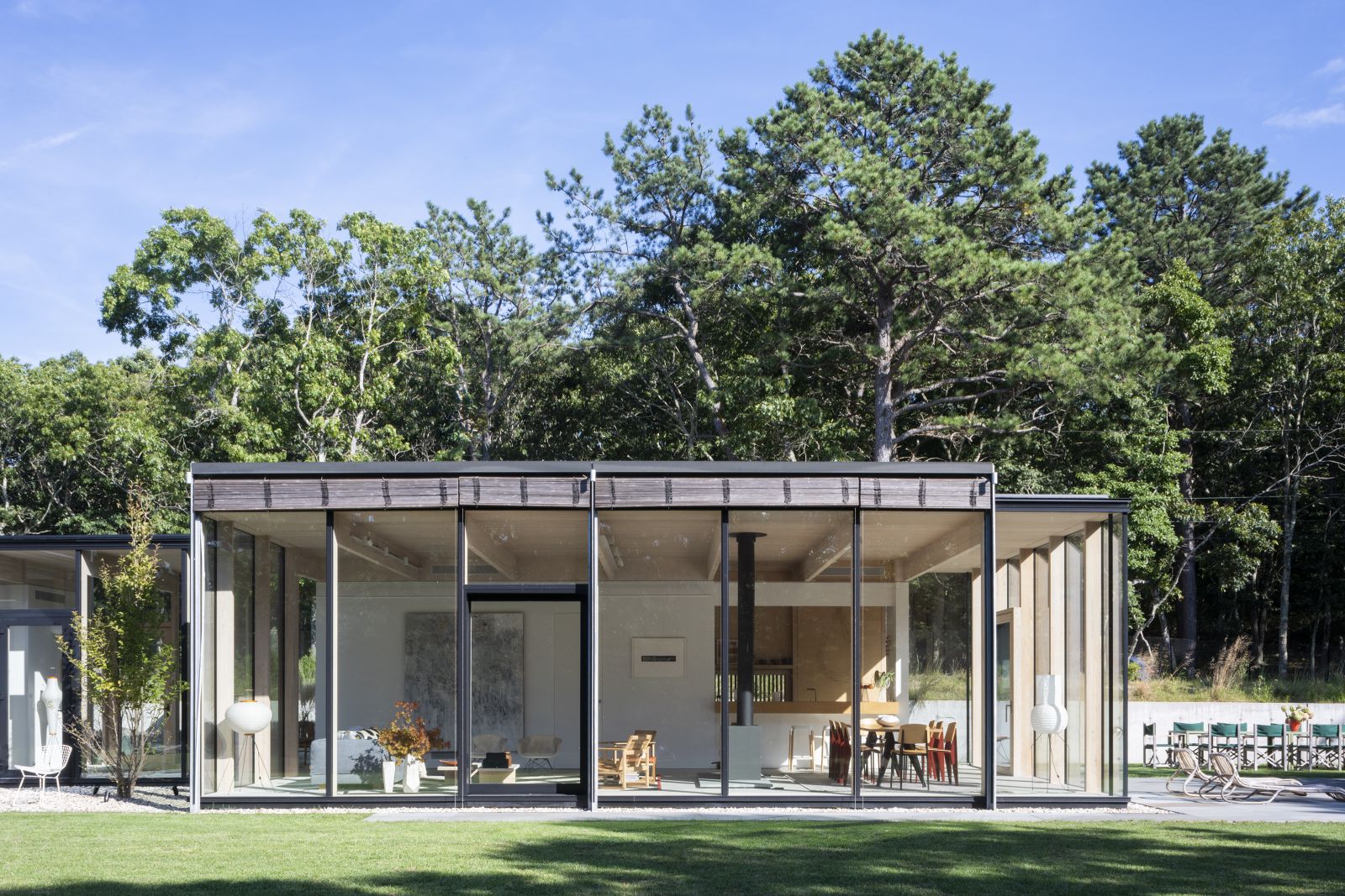 Dichter Eichenwald umrahmt das transparente Haus von allen Seiten. Der lange Bungalow besteht aus zwei Teilen: dem öffentlichen Bereich im Vordergrund und dem privaten Hausteil mit Schlafzimmern weiter hinten.