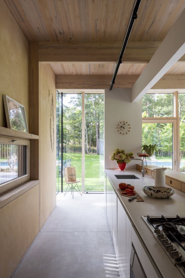 Der durchgängige Betonboden bildet einen bewussten Kontrast zu den hölzernen Elementen des Hauses. Eine Arbeitsplatte aus Corian und eine Frühstücksbar ergänzen die matt lackierten Küchenschränke von Minimal USA.