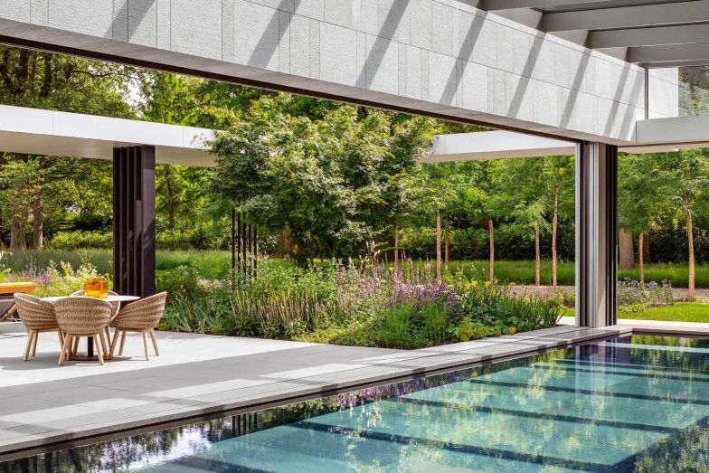 Die Bäume schirmen Haus und Pool, der im Sommer der schönste Ort des Hauses sein dürfte, perfekt ab. Das Becken verfügt über allerlei technische Raffinessen – darunter einen beweglichem Boden und bewegliche Glasfassaden. Stühle: «Sandua» von Robin Hapelt für Manutti.