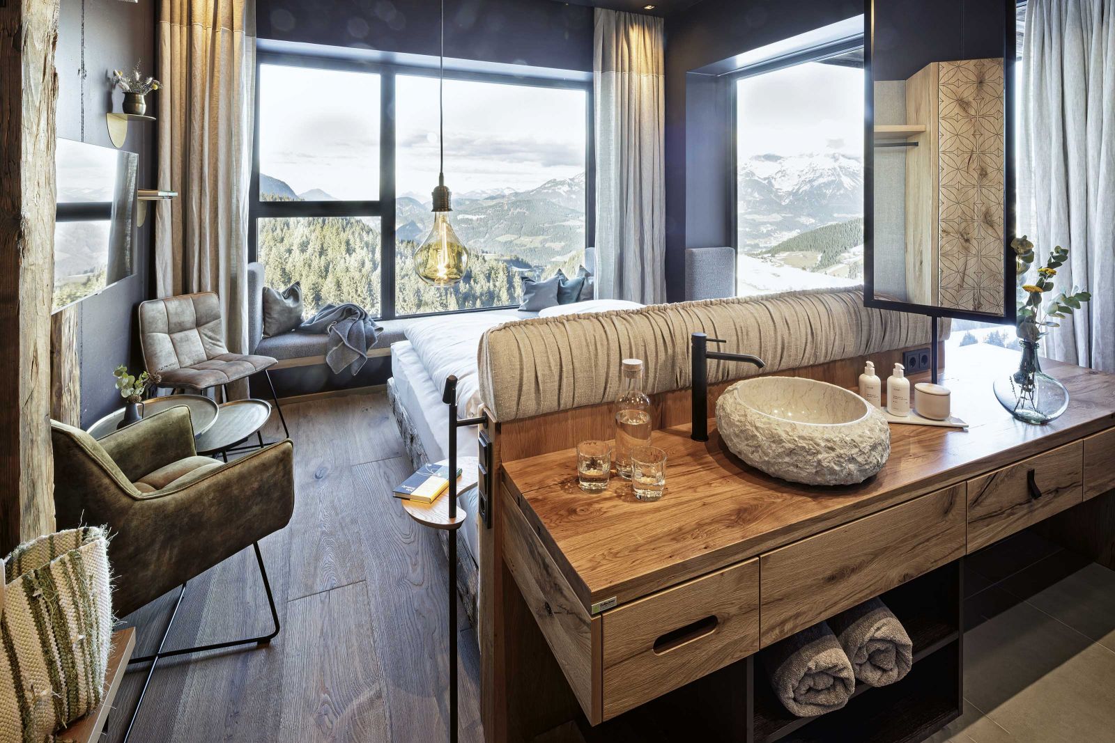 Panoramablick vom Bett aus: Die Zimmer sind echte Rückzugsplatzerl – chick und zugleich urgemütlich bieten sie, je nach Kategorie, eine freistehende Badewanne am Fenster, eine Sofalandschaft mit Wiesenduft oder Rundumgipfelblick, mit Abendrot oder Morgensonne.
