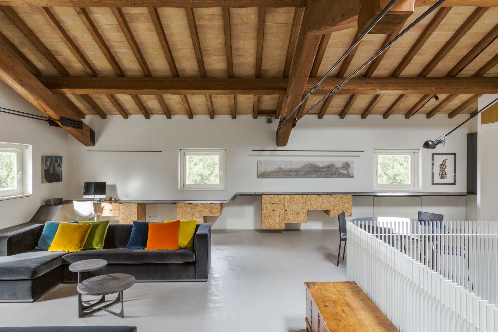 Das Mezzanin öffnet sich nun nach oben hin und gibt den Blick auf die Dachkonstruktion frei. Hier steht den Bauherren ein grosszügiger Homeoffice-Bereich zur Verfügung. Auffällig ist das raffinierte Metallband, dass durch den gesamten Raum läuft und mal Schreibtisch, Zeitungsständer oder schlicht Abstellfläche ist. Sofa: «Apta» von Antonio Citterio für Maxalto; Couchtisch: Opificio Lauchli; Wandleuchte von Flos.