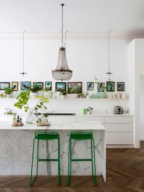 Selbst in der Küche bleibt die Hausherrin konsequent: Wände, Fronten und die Insel erstrahlen in Weiss und werden durch die grünen Barhocker von Hay und die indischen Glasmalereien an der Wand ergänzt. Selbst die Kombination von Kronleuchter und Industrieleuchten geben ein stimmiges Bild ab.