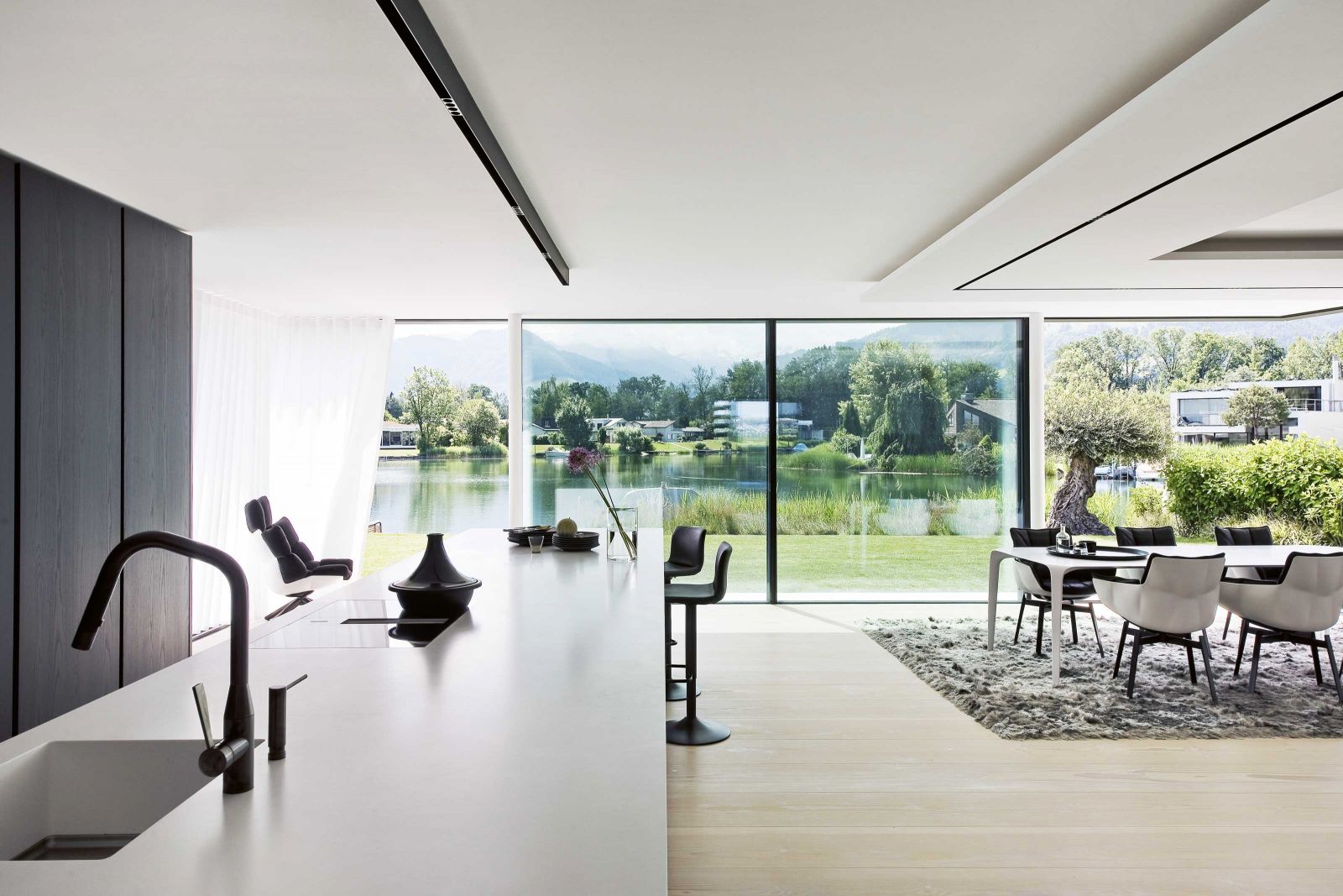 Was für ein Panorama: Nach Süden grenzt das Grundstück an eine geschützte Bucht mit direktem Zugang zum Zürichsee, im Hintergrund sind die von Wolken weichgezeichneten Berge zu sehen. Auf dem Boden wurden massive Dielen aus Douglasie verlegt, von Dinesen. Blickfang um den Esstisch sind die Schalensessel «Husk» der Designerin Patricia Urquiola für B&B Italia.