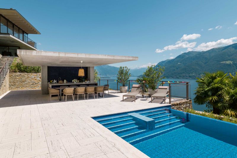 Unbestreitbarer Mittelpunkt der Sommertage und -abende ist der Infinity-Pool mit Sommerküche. Er liegt genau zwischen der Villa der Eigentümer und dem Ferienhaus für ihre Gäste. Möbel: Tisch «Air» von Koen Van Extergem für Manutti, Stühle «Bitta» von Rodolfi Dordoni & Liegen «Park Life» von Jasper Morrison für Kettal.