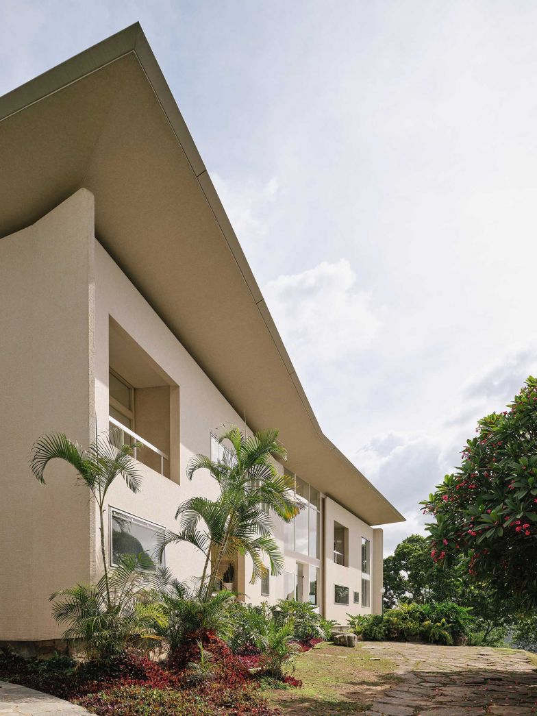 Die Fassade der Villa Planchart präsentiert sich als kühne Komposition aus Licht und Schatten. Das schwebende Dach, eine Skulptur für sich, scheint mit seinen präzise abgeschrägten Kanten der Schwerkraft zu trotzen. Grosszügige Öffnungen durchbrechen die weisse Fläche und lassen die Natur ins Haus. Wie ein eleganter Schmetterling ruht der Bau inmitten der tropischen Vegetation, die ihn sanft umschliesst.