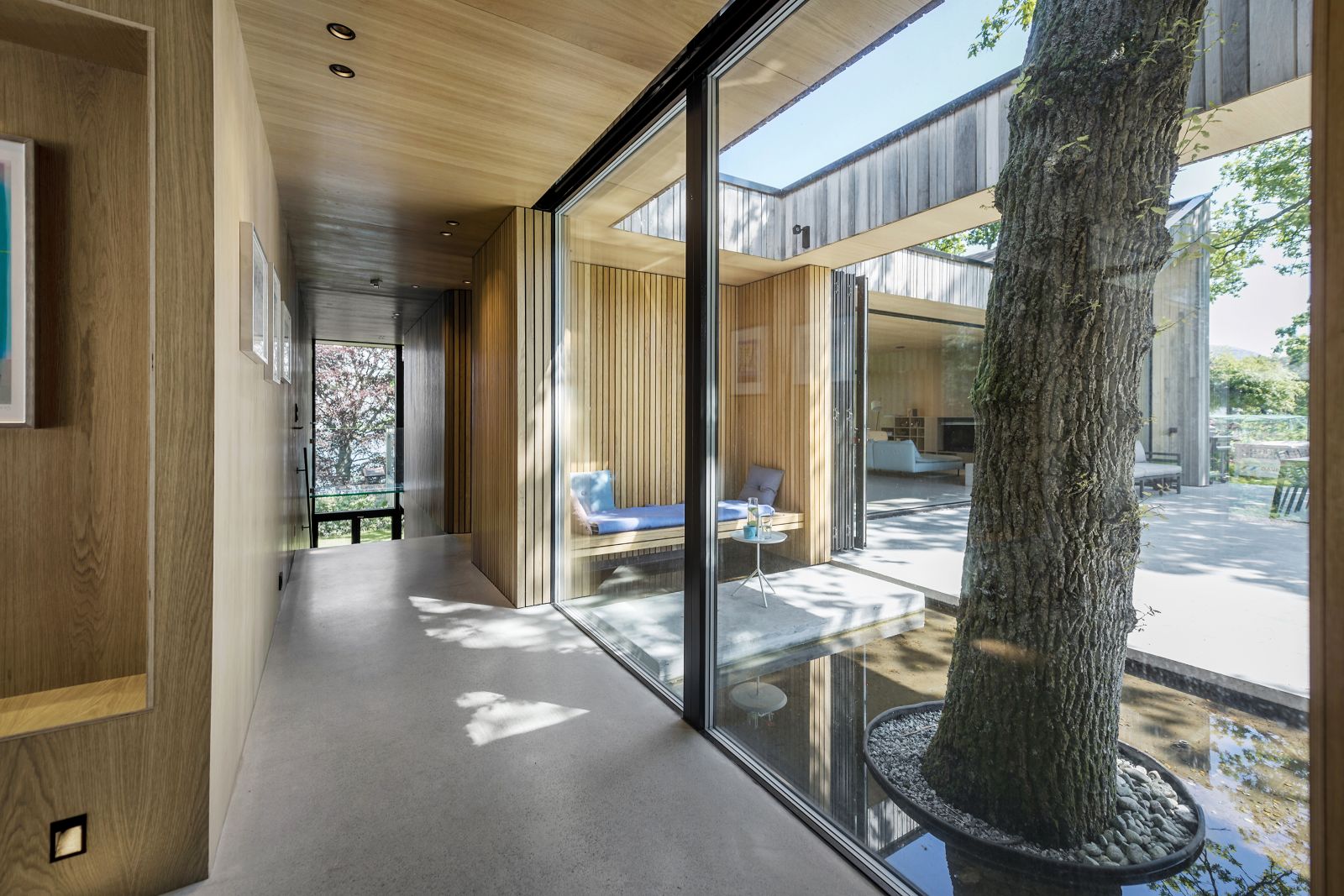 Eine der Eichen auf dem Grundstück wurde in die Planung einbezogen. Der Eigentümer hätte den Baum gern im Haus gehabt, aber das ist in Norwegen nicht erlaubt. Es musste eine Lösung her, bei der die Eiche draussen blieb. Nun vermittelt ein Wasserspiegel rund um den Baum und eine Sitzecke das Gefühl, sie stehe im Haus.