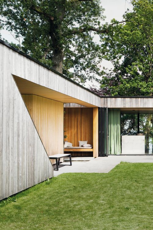 Dort, wo die Fassade Wind und Wetter nicht zu stark ausgesetzt ist, besitzt das Holz noch seine goldenen Nuancen. Die zweite Etage ist nicht von überall her ersichtlich. Der Architekt behauptete sich und überzeugte das Paar, nicht nach oben zu bauen, sondern das Haus in den Boden zu senken, sodass es geschützt zwischen den Bäumen, statt über ihnen steht.