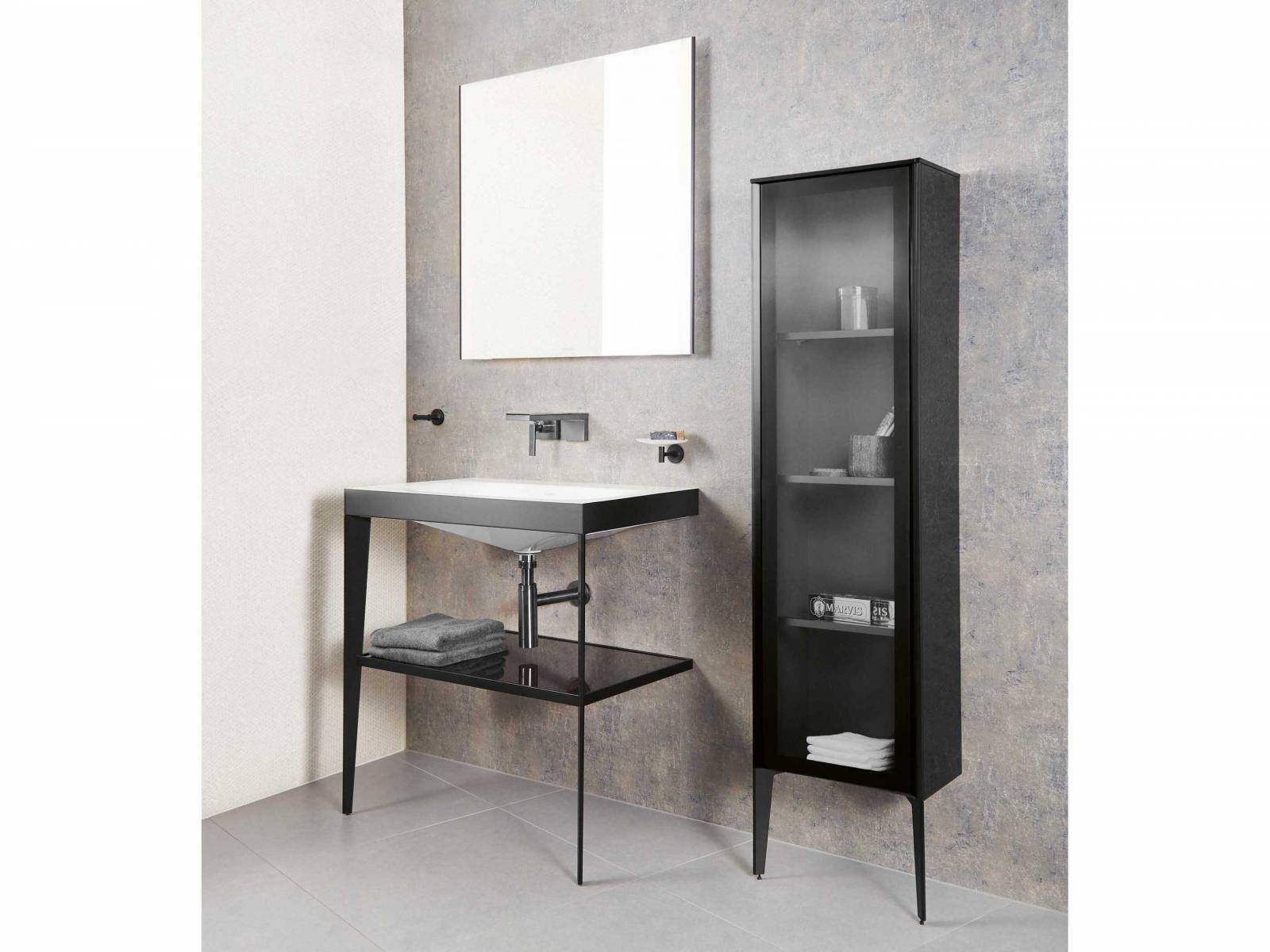 Das elegante Schwarz der Badmöbel ist in diesem Fall bloss einer der Schlankmacher. Regal und Schrank besitzen jeweils nur zwei Beine und sind rückseitig an der Wand befestigt. Das spart Platz, wenn er rar ist und wirkt mit kraftvollen Linien ebenso im geräumigen Bad. Der grosszügige Lichtspiegel und das breite Lavabo erleichtern das Handling. Sabag.