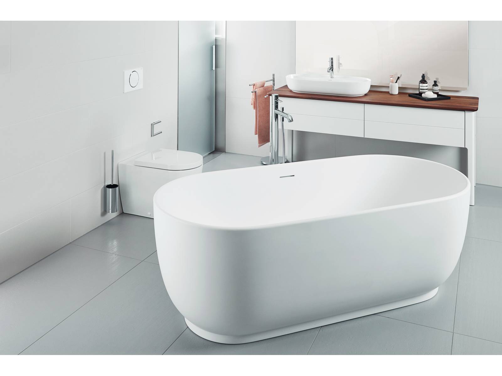 Das nüchterne Bad in schlichtem Grauweiss bildet die perfekte Bühne für die freistehende Badewanne. Für eine einladende Atmosphäre sorgt die Konsole aus amerikanischen Nussbaum. Sabag.