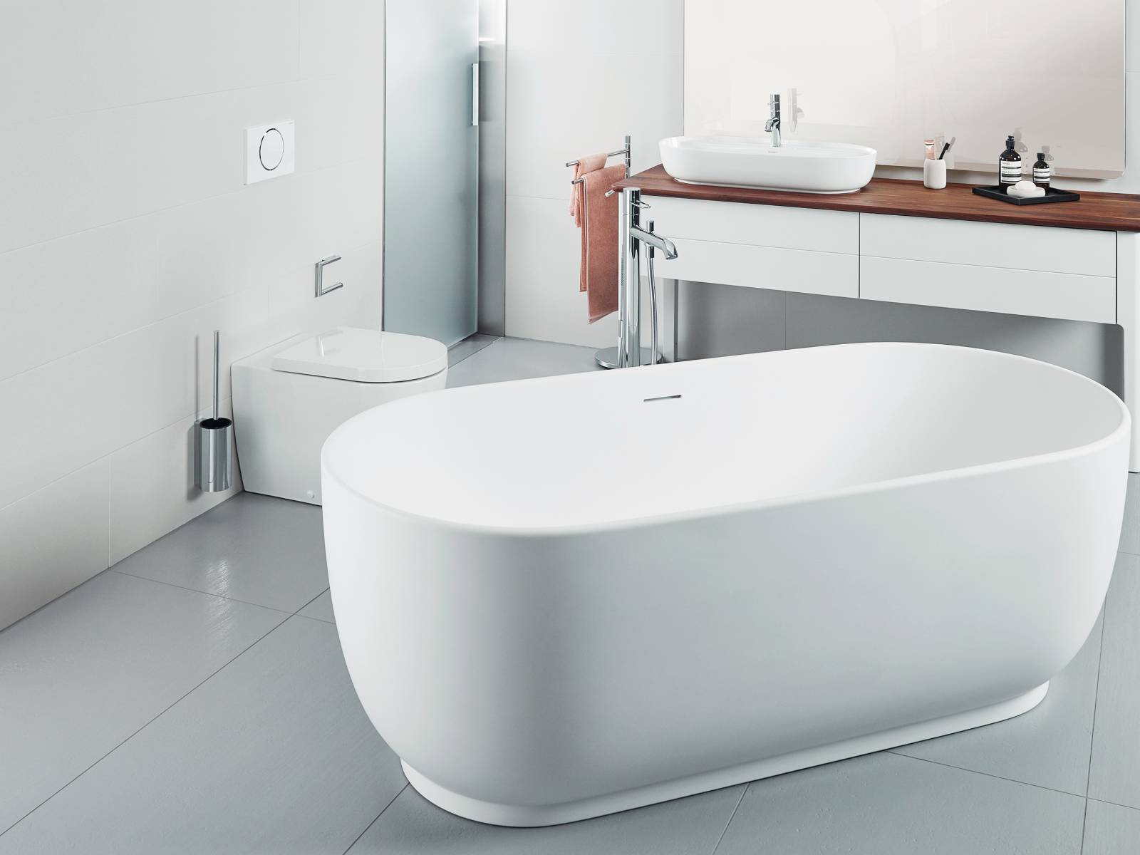 Das nüchterne Bad in schlichtem Grauweiss bildet die perfekte Bühne für die freistehende Badewanne. Für eine einladende Atmosphäre sorgt die Konsole aus amerikanischen Nussbaum. Sabag.