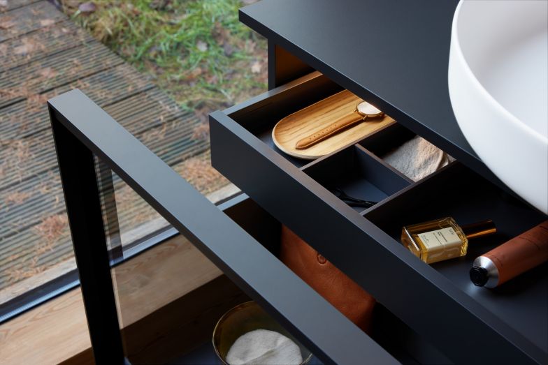 Eine horizontale, in den Metallrahmen integrierte Griffleiste vervollständigt das reduzierte Möbel mit einem Auszug.