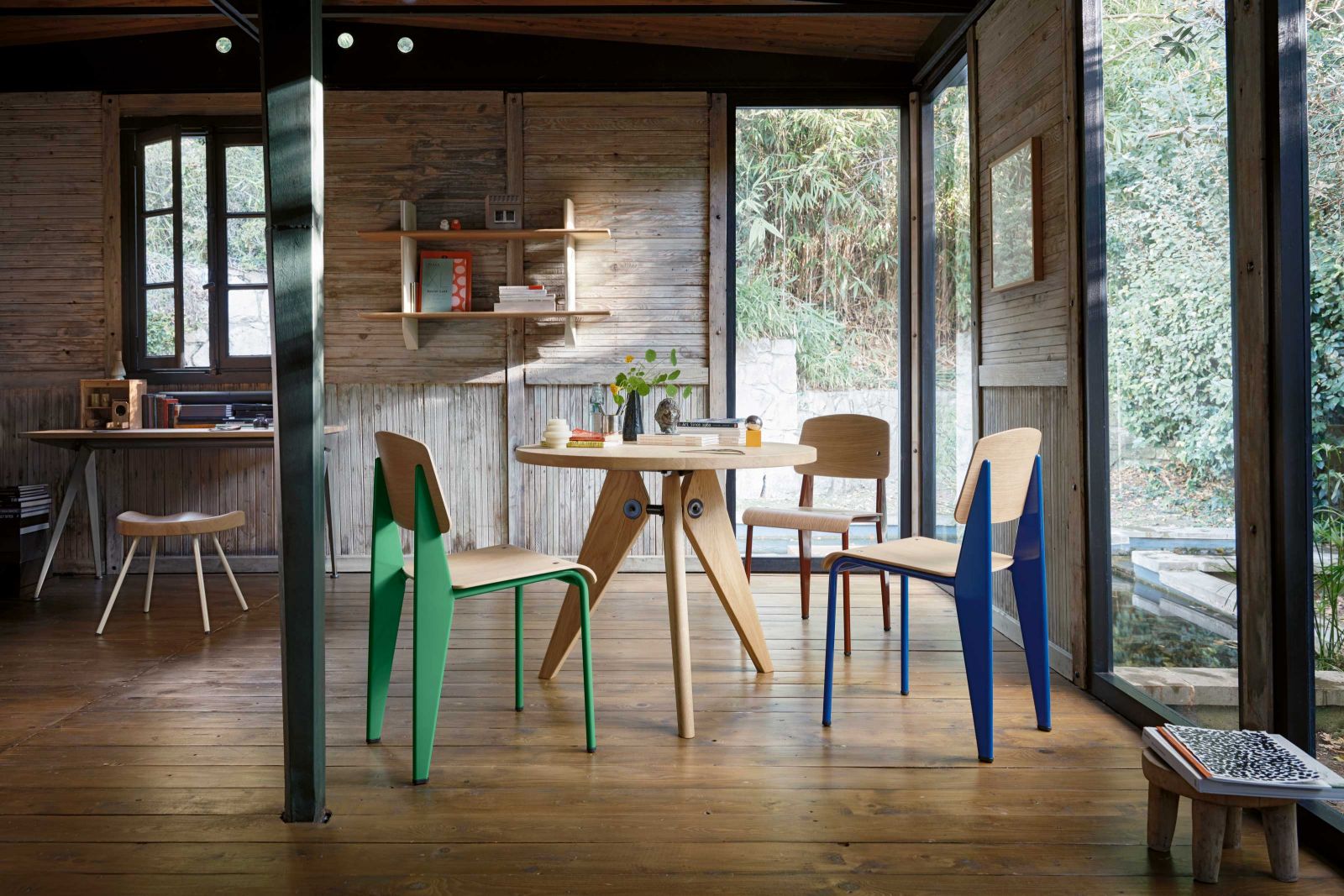 Blick in ein Demountable House mit Wandregal «Mural», Esstisch «Guéridon», den Stühlen «Standard» (in den neuen Farben Blé Vert, Japanese Red und Bleu Marcoule) sowie links der Hocker «No. 307»