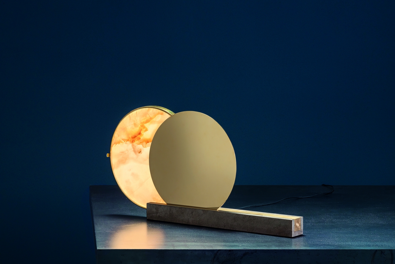 «Alchemie T» spielt mit dem Gegensatz von Licht und Dunkelheit, von Sonne und Mond: Mit einer leichten Berührung der Hand wird die Messingscheibe zum Gleiten gebracht bis sich beide Scheiben wie bei einer Sonnenfinsternis überlappen. Für ein ganz besonders Ambiente sorgt diese skulpturale Tischleuchte, da Form und Lichtintensität durch Bewegung verändert werden können. Cattelani & Smith.