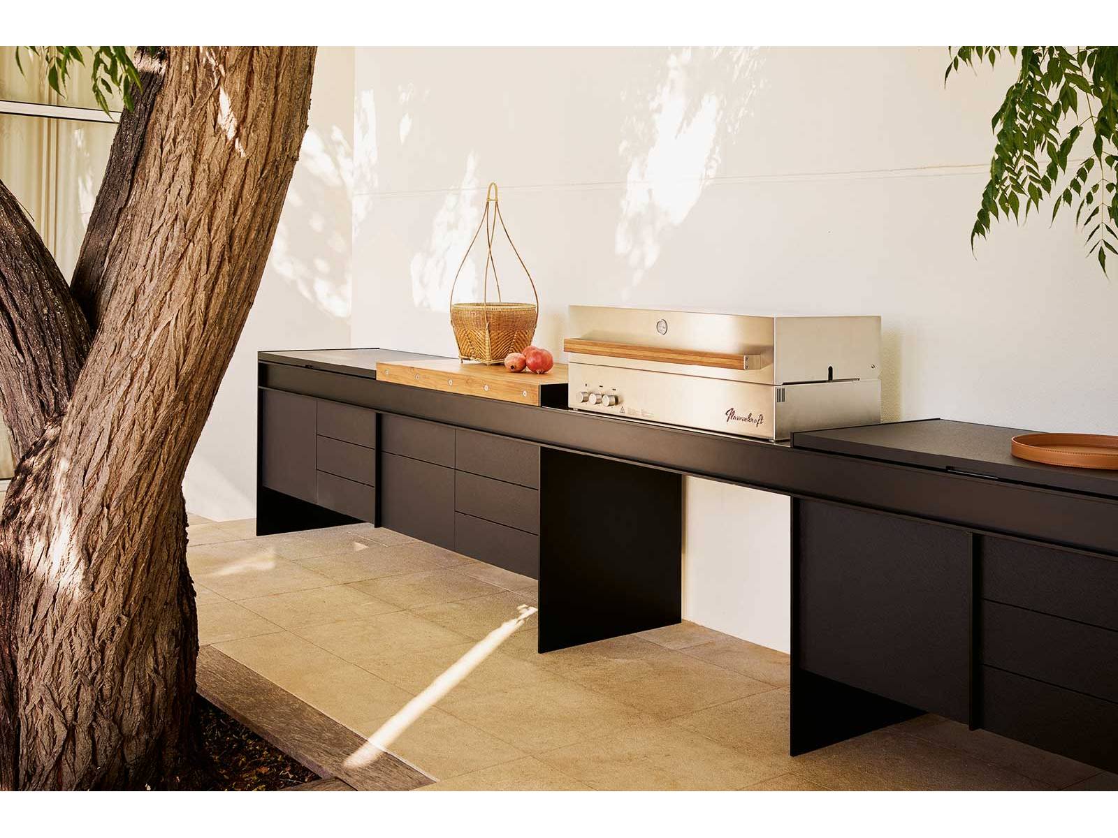 Die erste Outdoor-Küche des italienischen Herstellers besticht durch ihre schwebende Ästhetik. Diese wird durch eine raffinierte Brückenstruktur aus mattschwarz lackiertem Aluminium erzeugt, an der die Aufbewahrungselemente scheinbar schwerelos hängen. Poliform.