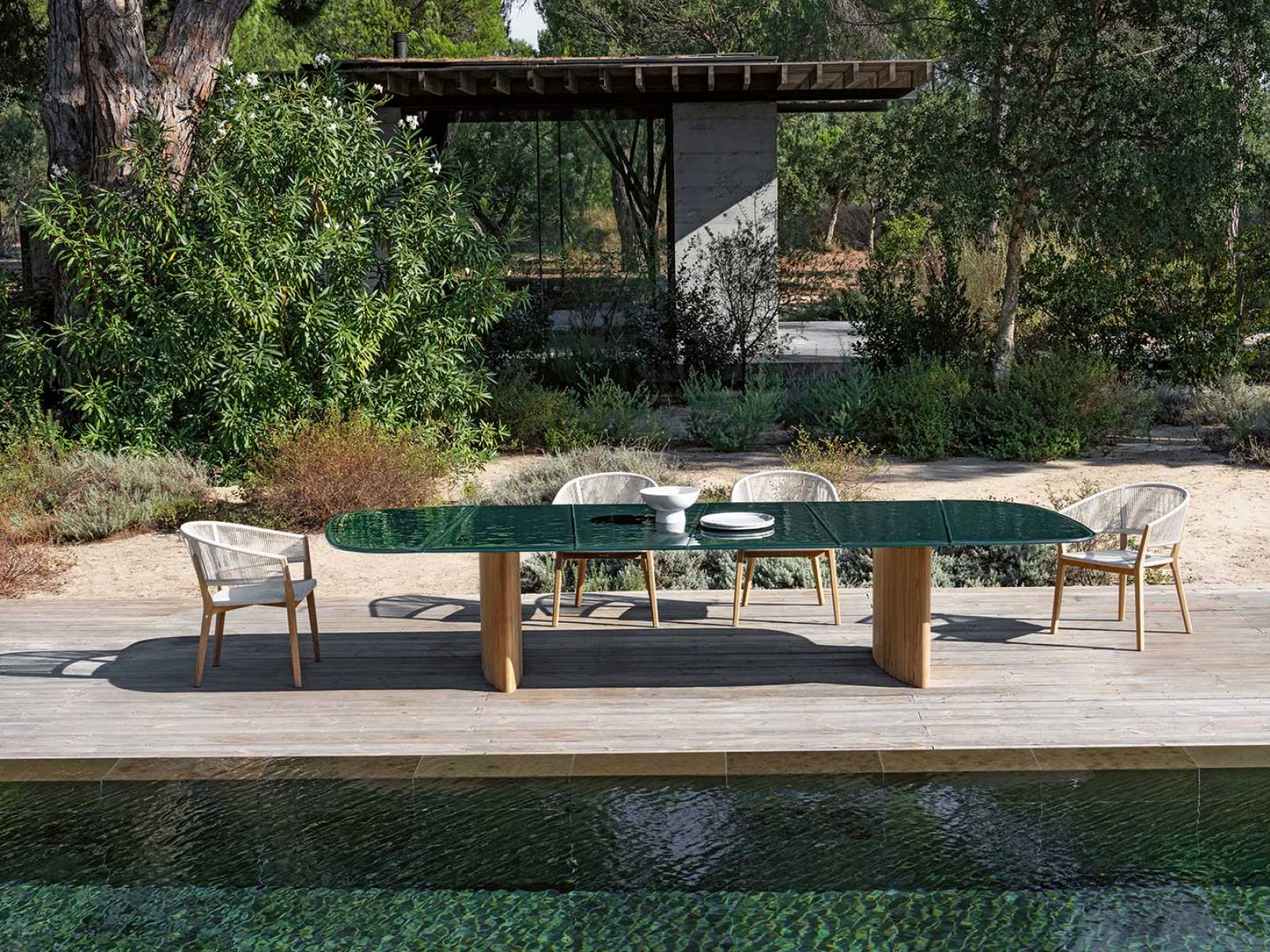 Der Tisch «Regaliz» von Kris Van Puyvelde feiert den Luxus unter freiem Himmel. Seine Glasplatte, kunstvoll verschmolzen und in edlen Farbtönen wie Dunkelgrün, -braun oder Pebble schimmernd, fängt das Licht ein wie eine Bühne. Darunter: massive Beine aus Teak.  ROYAL BOTANIA.