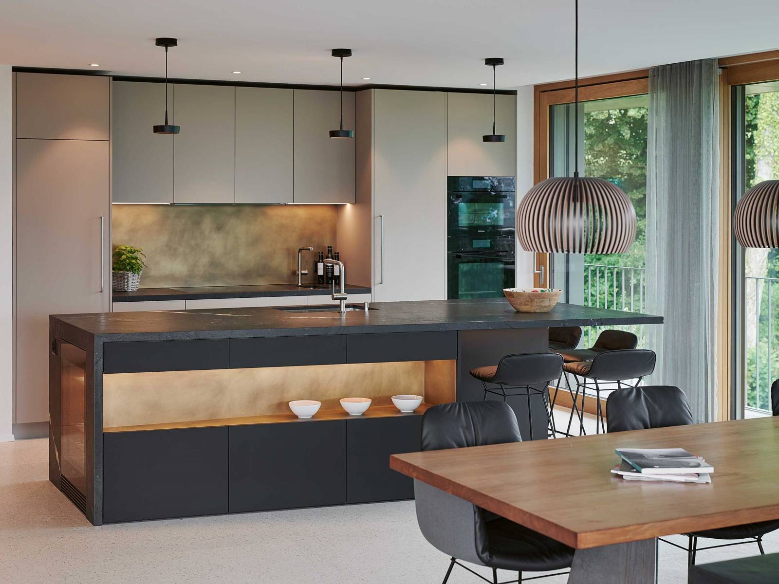 Hello Darkness: Schwarz hat längst auch die Küche erobert. Hier als stylische Kochinsel, der naturgrau gehaltene Hochschränke beistehen. Als verbindendes Element dienen die Nischen aus Messing. Ein weiteres Highlight ist die Arbeitsplatte aus Naturstein, deren Oberfläche den Eindruck von Leder erweckt. BRUNNER KÜCHEN.