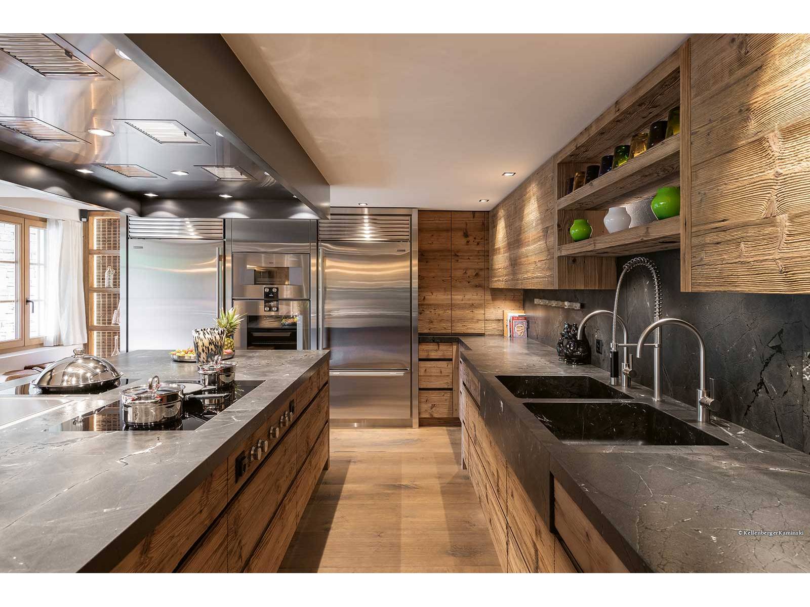 Handwerk und Material verschmelzen in dieser Küche zu einer stimmigen Einheit: In sorgfältiger Schreinerarbeit aus charaktervollem Altholz gefertigt, trifft die dunkel geäderte Natursteinabdeckung auf klare Linien und eine präzise Fugenführung. Die ruhige Gestaltung legt den Fokus auf die Qualität des Materials und die Präzision des Ausbaus. ZBAEREN.