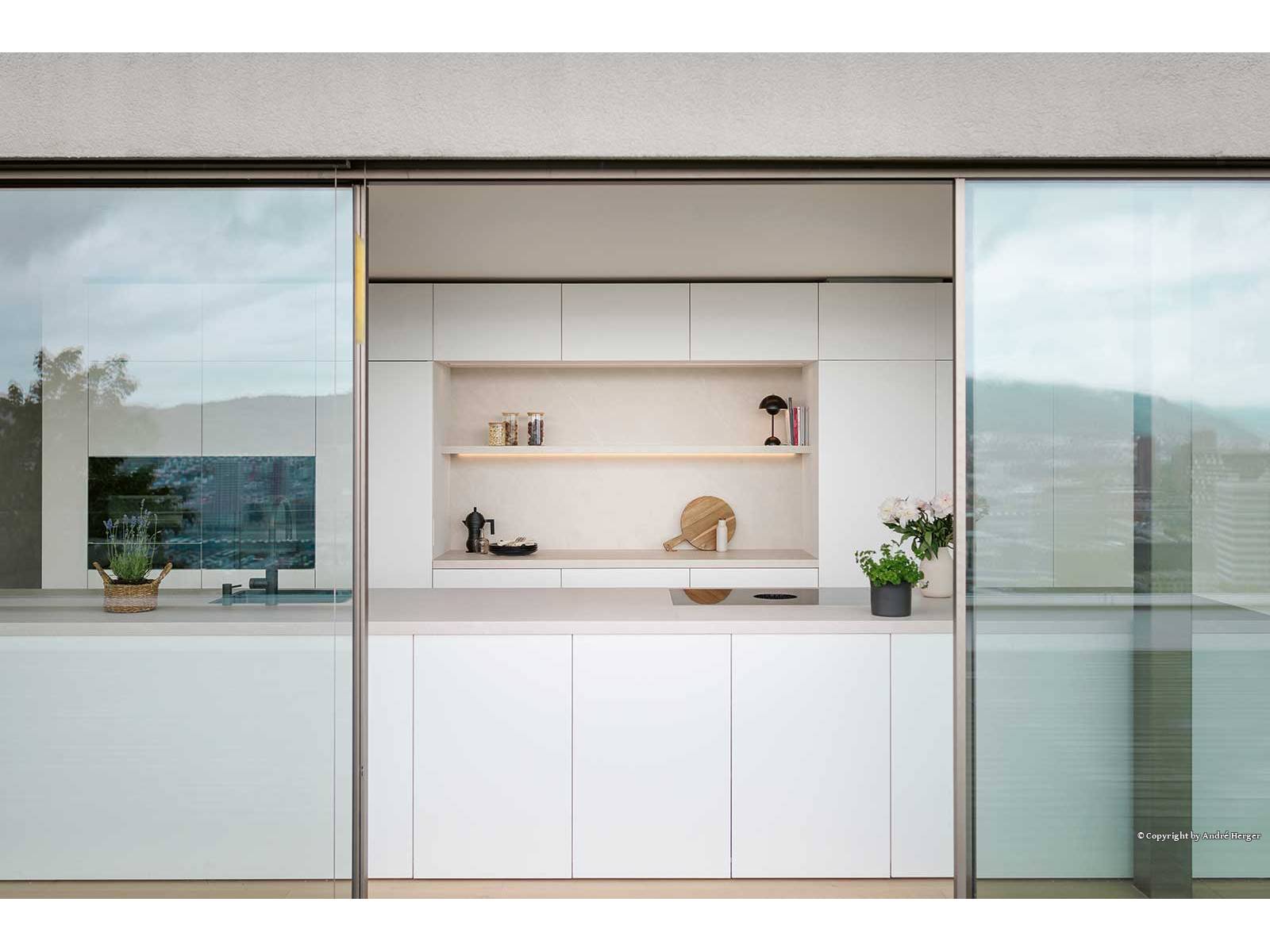 Die grifflose Küche aus der Produktfamilie «Nova» überzeugt mit ultramatter, samtigweicher Oberfläche, die dank Anti-Fingerprint-Technologie dauerhaft gepflegt bleibt. Sie umspielt offene, beleuchtete Regale, die für wohnliche Akzente sorgen. Die grosszügige Arbeitsfläche bietet Platz für gemeinsames Kochen, während Schiebe­türen den Innenraum nahtlos nach draussen führen. ­Präzise Linienführung, hochwertige Materialien und ­un­aufdringliche Integration von Geräten schaffen eine zeitlose Eleganz. VERISET.