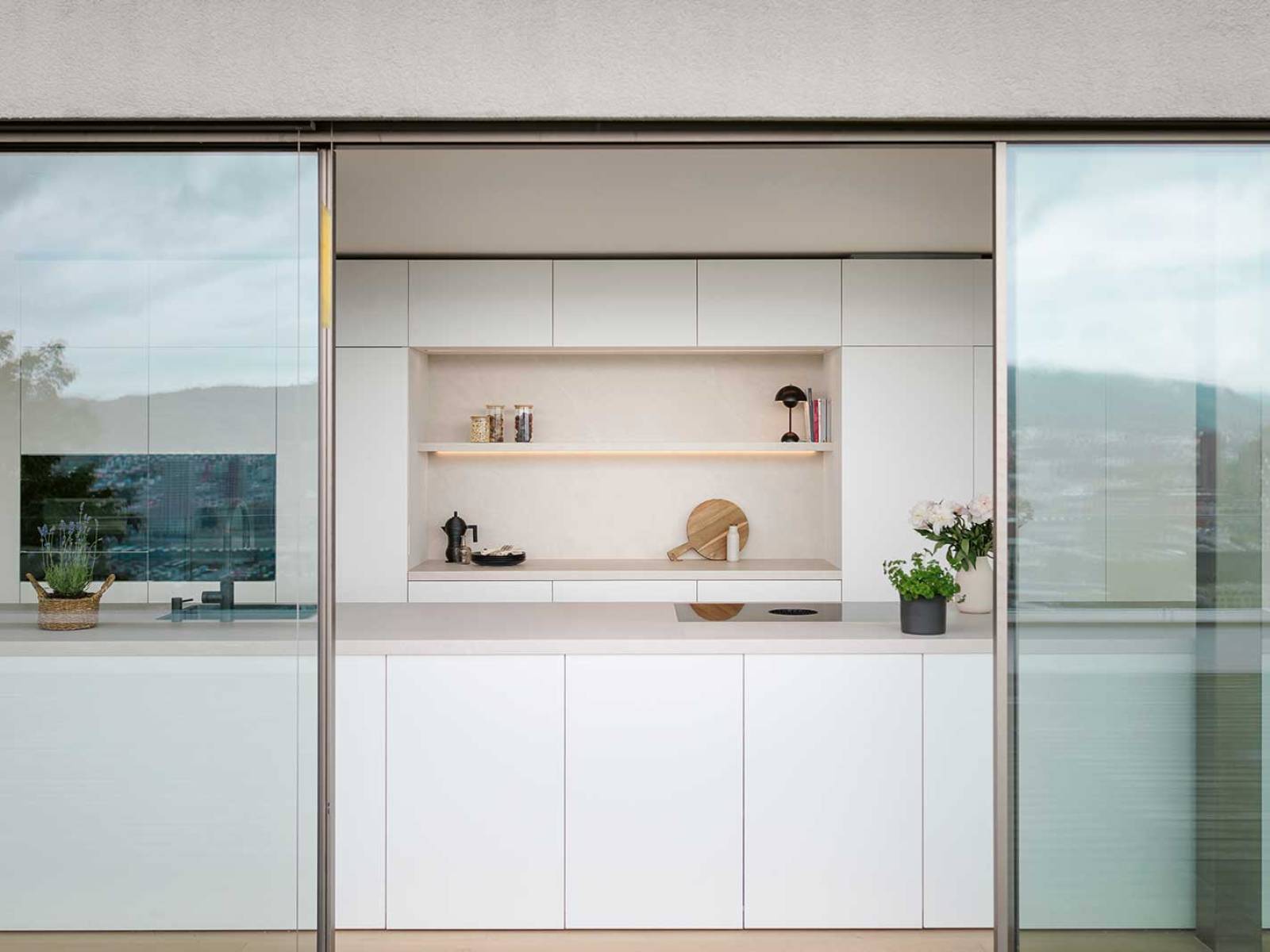 Die grifflose Küche aus der Produktfamilie «Nova» überzeugt mit ultramatter, samtigweicher Oberfläche, die dank Anti-Fingerprint-Technologie dauerhaft gepflegt bleibt. Sie umspielt offene, beleuchtete Regale, die für wohnliche Akzente sorgen. Die grosszügige Arbeitsfläche bietet Platz für gemeinsames Kochen, während Schiebe­türen den Innenraum nahtlos nach draussen führen. ­Präzise Linienführung, hochwertige Materialien und ­un­aufdringliche Integration von Geräten schaffen eine zeitlose Eleganz. VERISET.