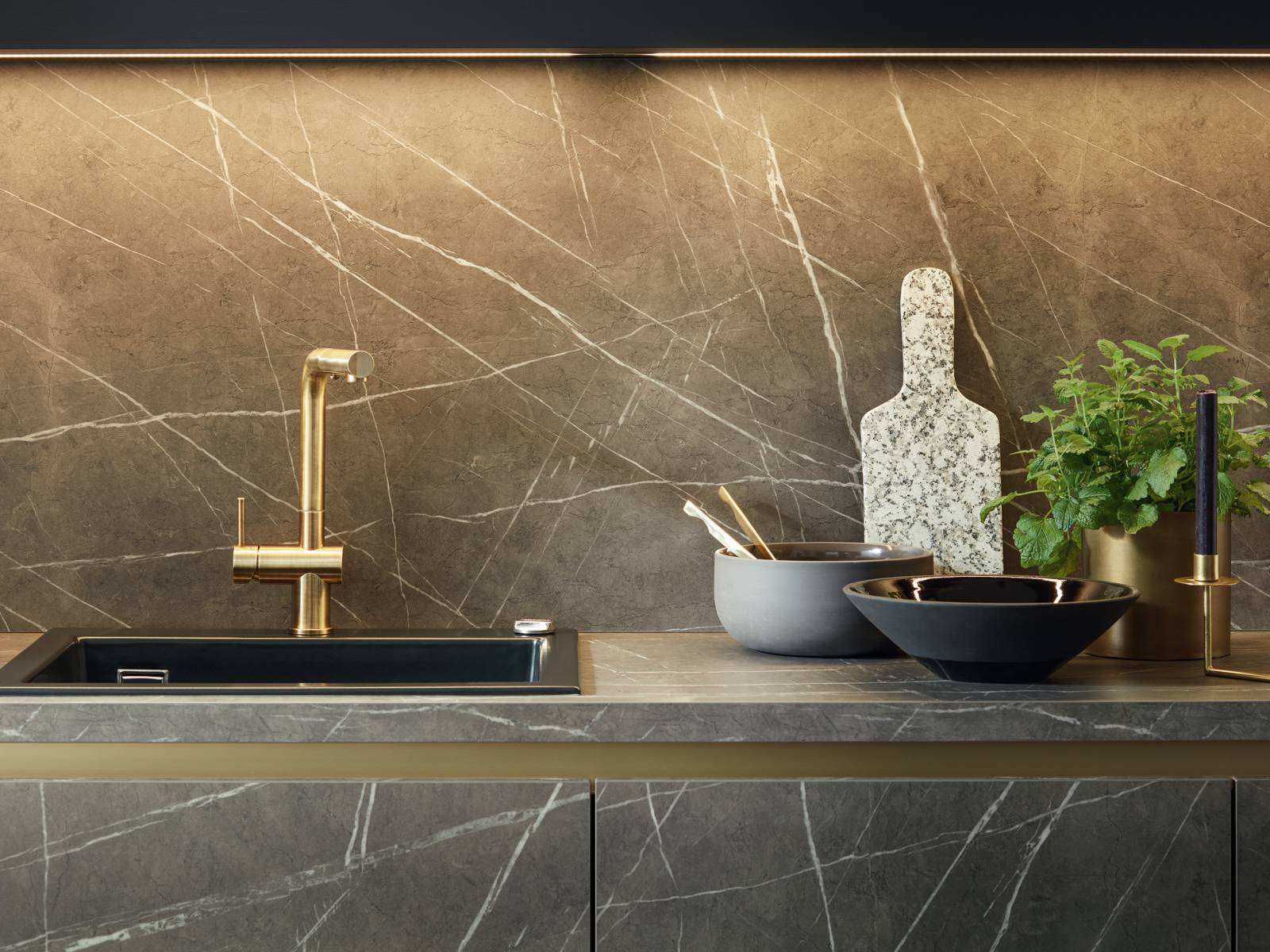 Zeitlos und dennoch topaktuell sind die eleganten Oberflächen aus der Targa-Linie, hier in dunklem Marmordekor, die durch ihre feine Maserung einen exklusiven Kontrast zu den edlen Messingdetails setzen. Schüller.