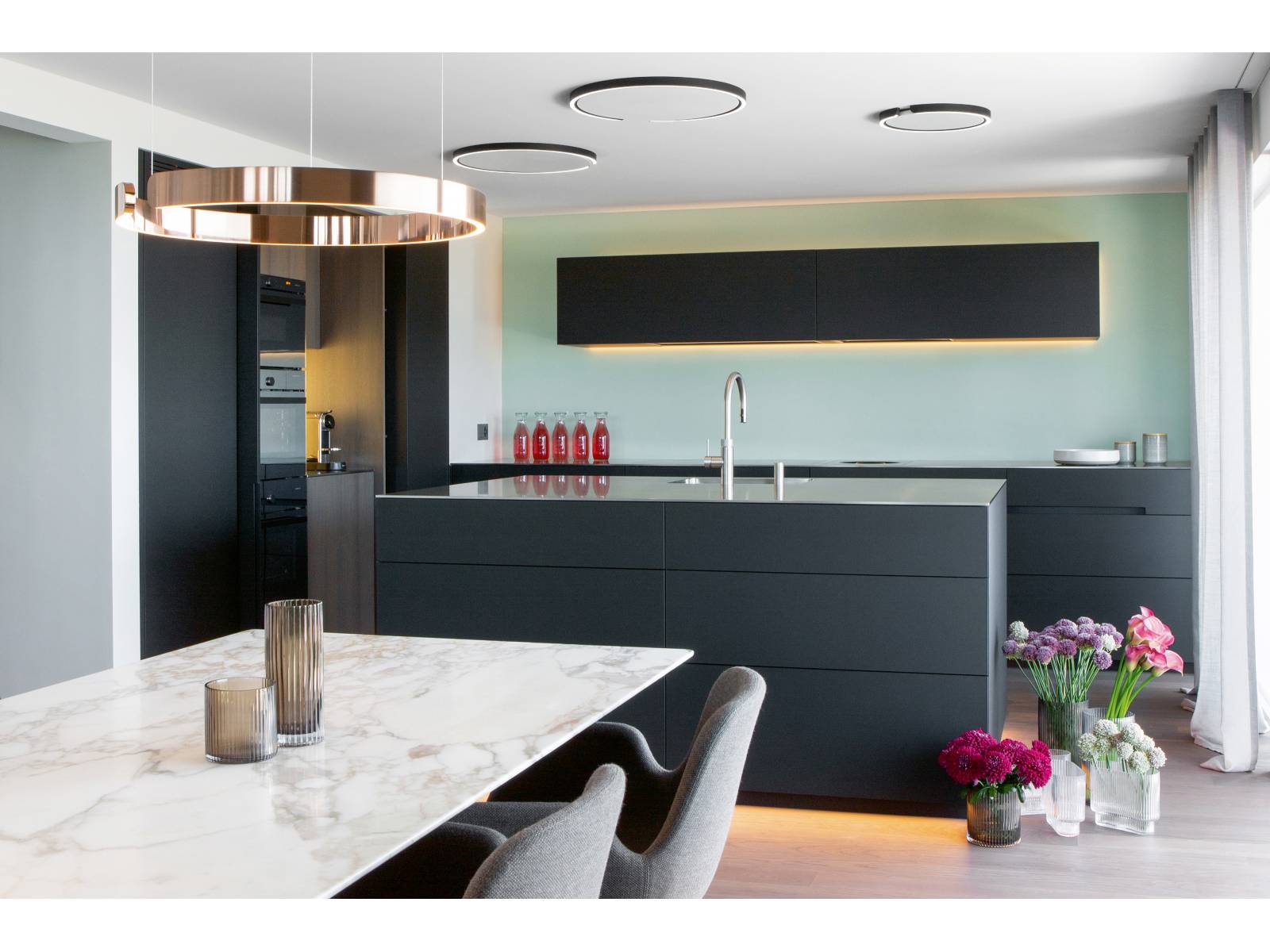 Eine schlichte Küche im minimalistischen Design, die mit raffinierten Details überzeugt: Eingefräste Griffe, matte MDF-Fronten, Dreheinschubtüren sowie raffiniert platzierte LED-Elemente, welche dem Inselblock und Oberbau eine schwebende Wirkung verleihen. Jede Küche dieser Manufaktur ist ein Unikat und wird in Appenzell hergestellt. Elbau.