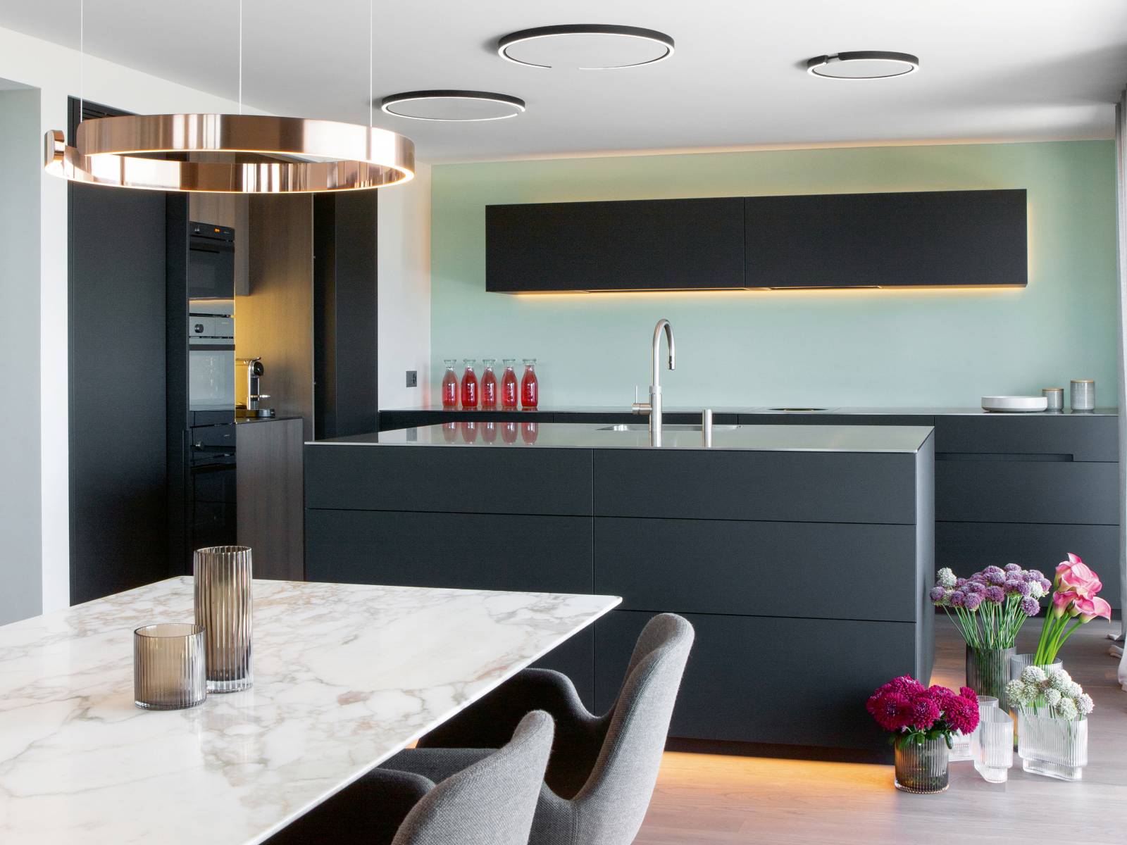 Eine schlichte Küche im minimalistischen Design, die mit raffinierten Details überzeugt: Eingefräste Griffe, matte MDF-Fronten, Dreheinschubtüren sowie raffiniert platzierte LED-Elemente, welche dem Inselblock und Oberbau eine schwebende Wirkung verleihen. Jede Küche dieser Manufaktur ist ein Unikat und wird in Appenzell hergestellt. Elbau.