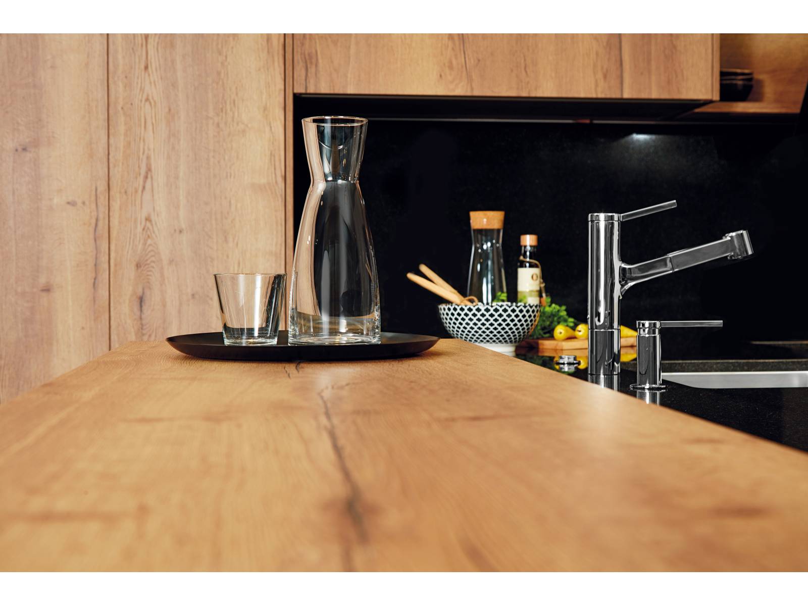 Elemente in Holzoptik erzeugen zusammen mit der eleganten Granitabdeckung eine moderne Herzlichkeit, die zum Ankommen und Verweilen einlädt. Diese Materialkombination ist bezeichnend für die Küche Typ «hochmodern», deren technisches Highlight ein Kochfeld mit intelligenter Dunstabzugshaube ist, die per Handy oder Tablet gesteuert werden kann. Sabag.