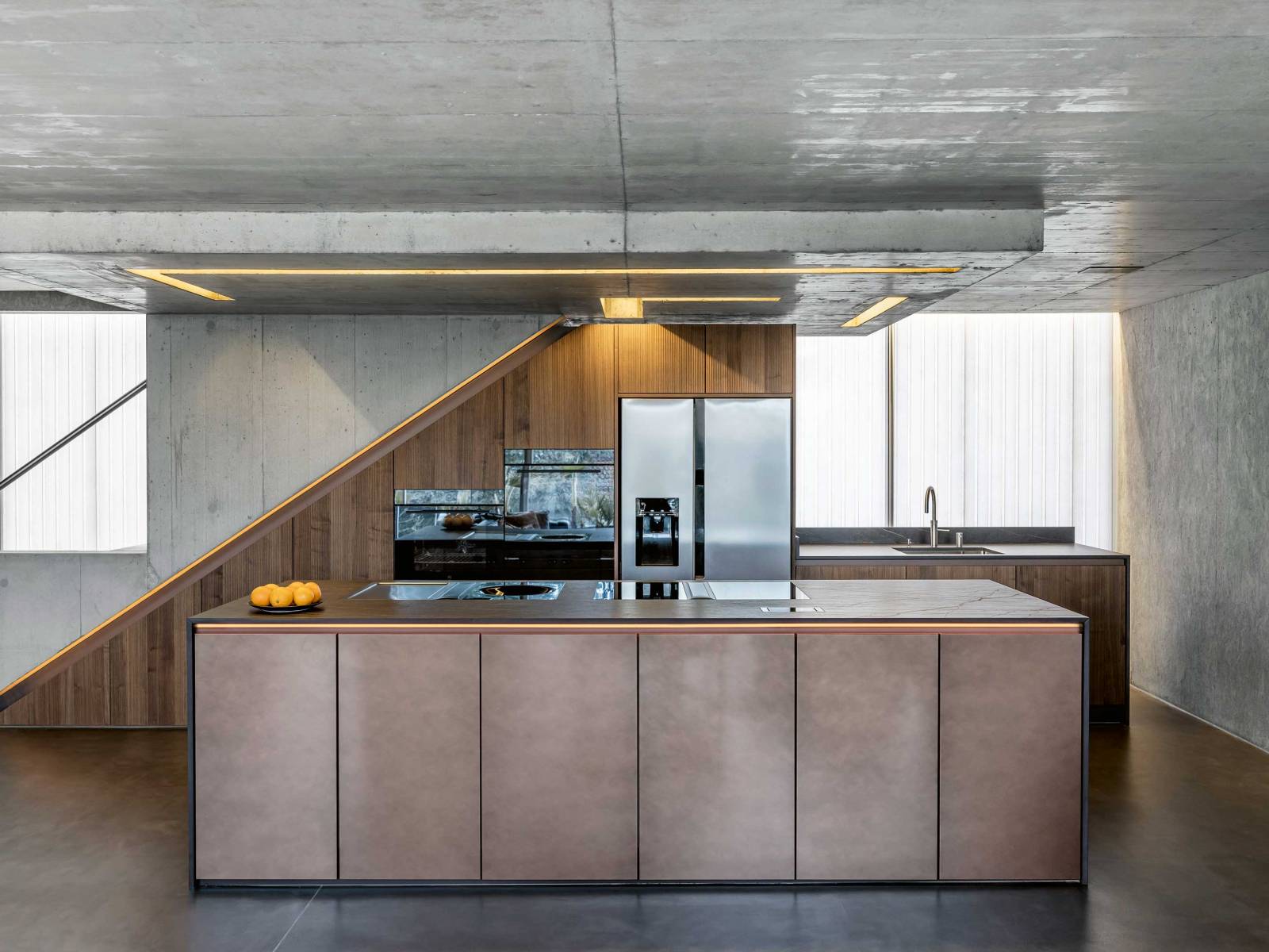 Es ist das Zusammenspiel der Materialien, das diese Küche zu einem Blickfang macht: Die gerillten Fronten aus Echtholzfurnier har­­­monieren mit denen der Kücheninsel in speziellem Metalldesign. Die dunkelbraune Arbeitsplatte ist mit goldenen Adern durchzogen, was bei der Beleuchtung farblich aufgenommen wurde. Gleich­­zeitig bildet die Küche einen spannenden Kontrast zum Sichtbeton und strahlt Wärme und Gemütlichkeit aus. SANITAS TROESCH.