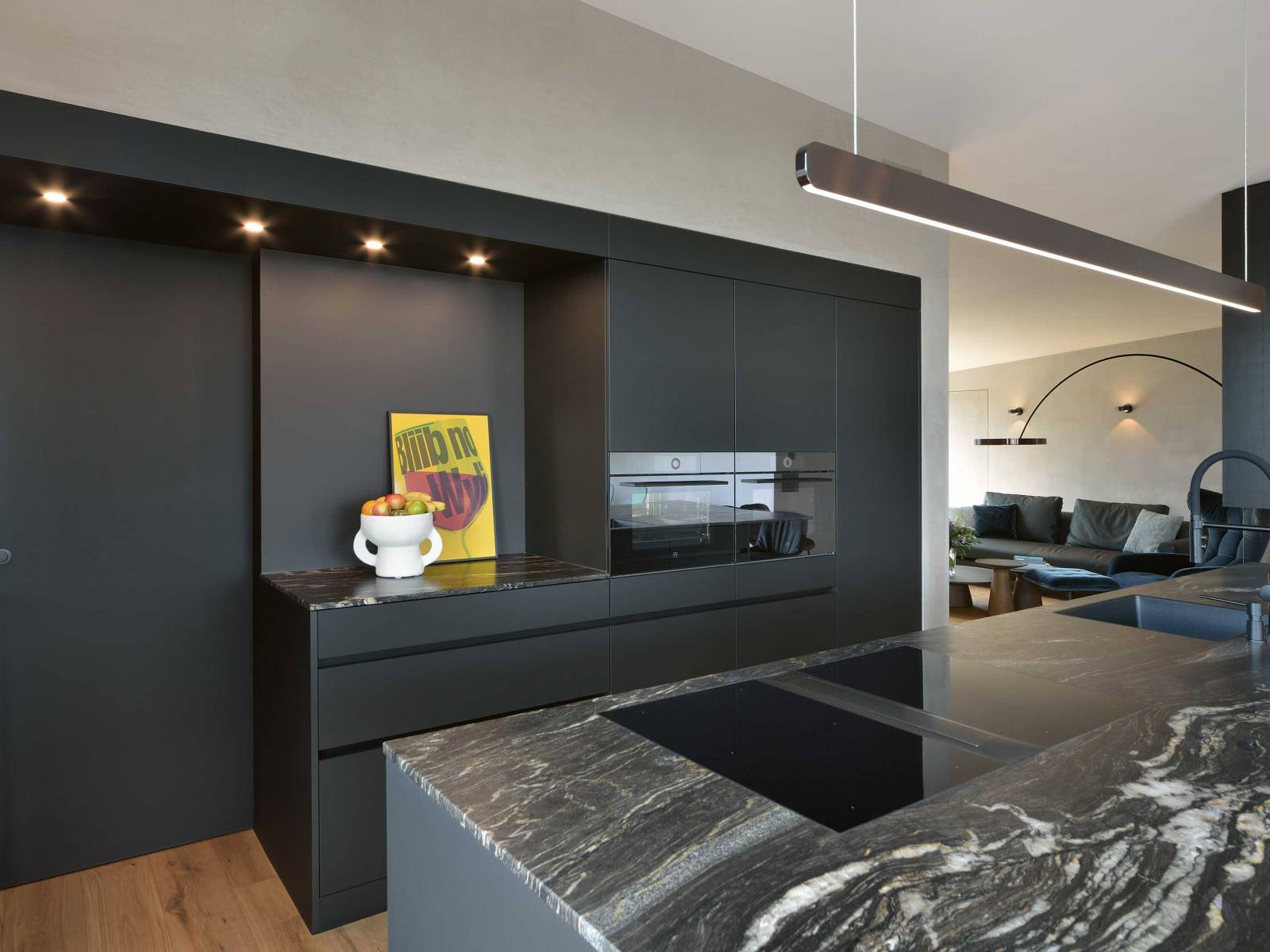 Schwarze Küchen sind nicht länger eine Seltenheit. Highlight in diesem Beispiel ist der Durchgang zum dahinterliegenden Reduit, der von einem L-förmigen Rahmen umfasst wird, auf dessen Seite sich eine Vitrine verbirgt. VERISET.
