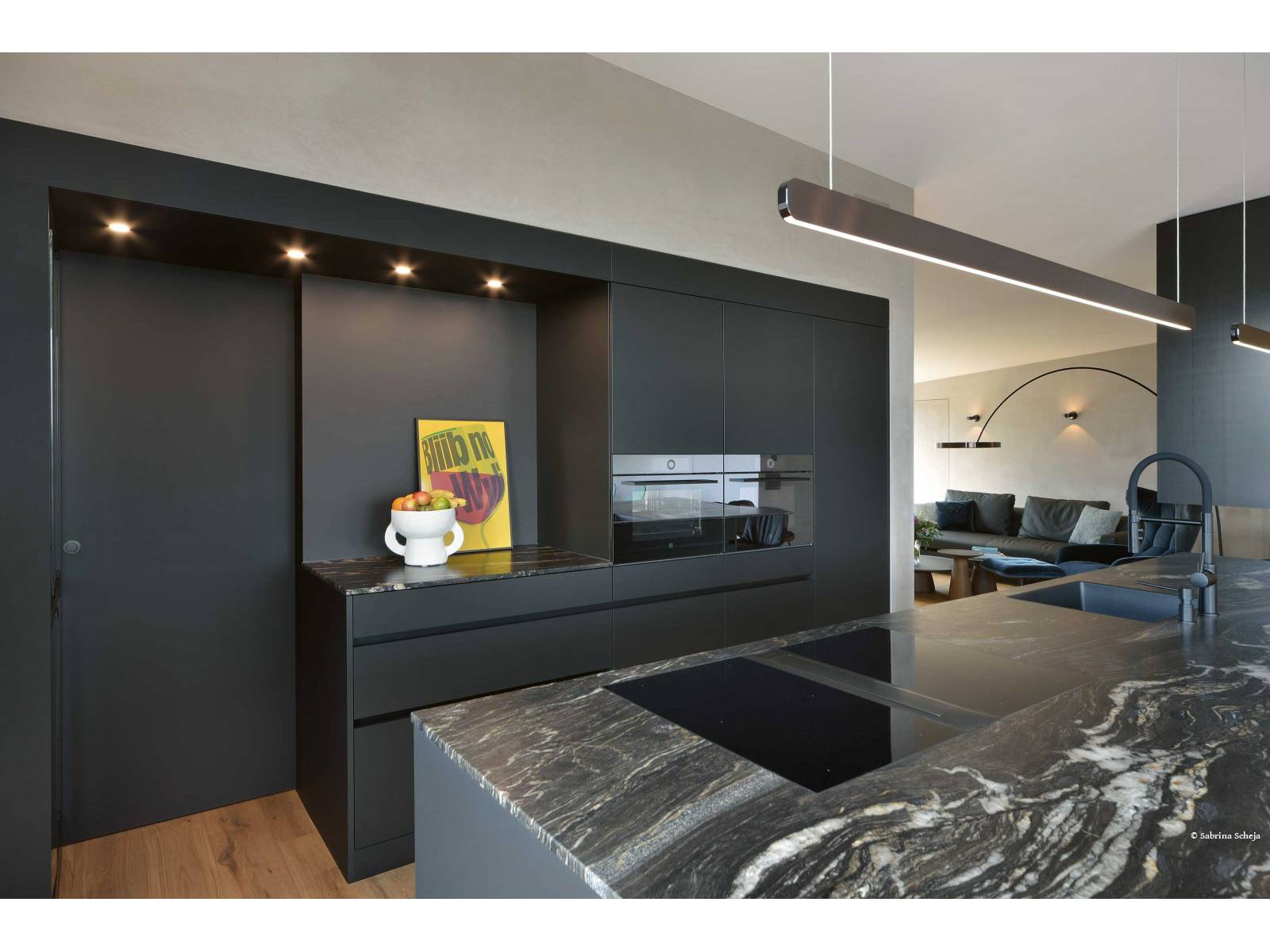 Schwarze Küchen sind nicht länger eine Seltenheit. Highlight in diesem Beispiel ist der Durchgang zum dahinterliegenden Reduit, der von einem L-förmigen Rahmen umfasst wird, auf dessen Seite sich eine Vitrine verbirgt. VERISET.