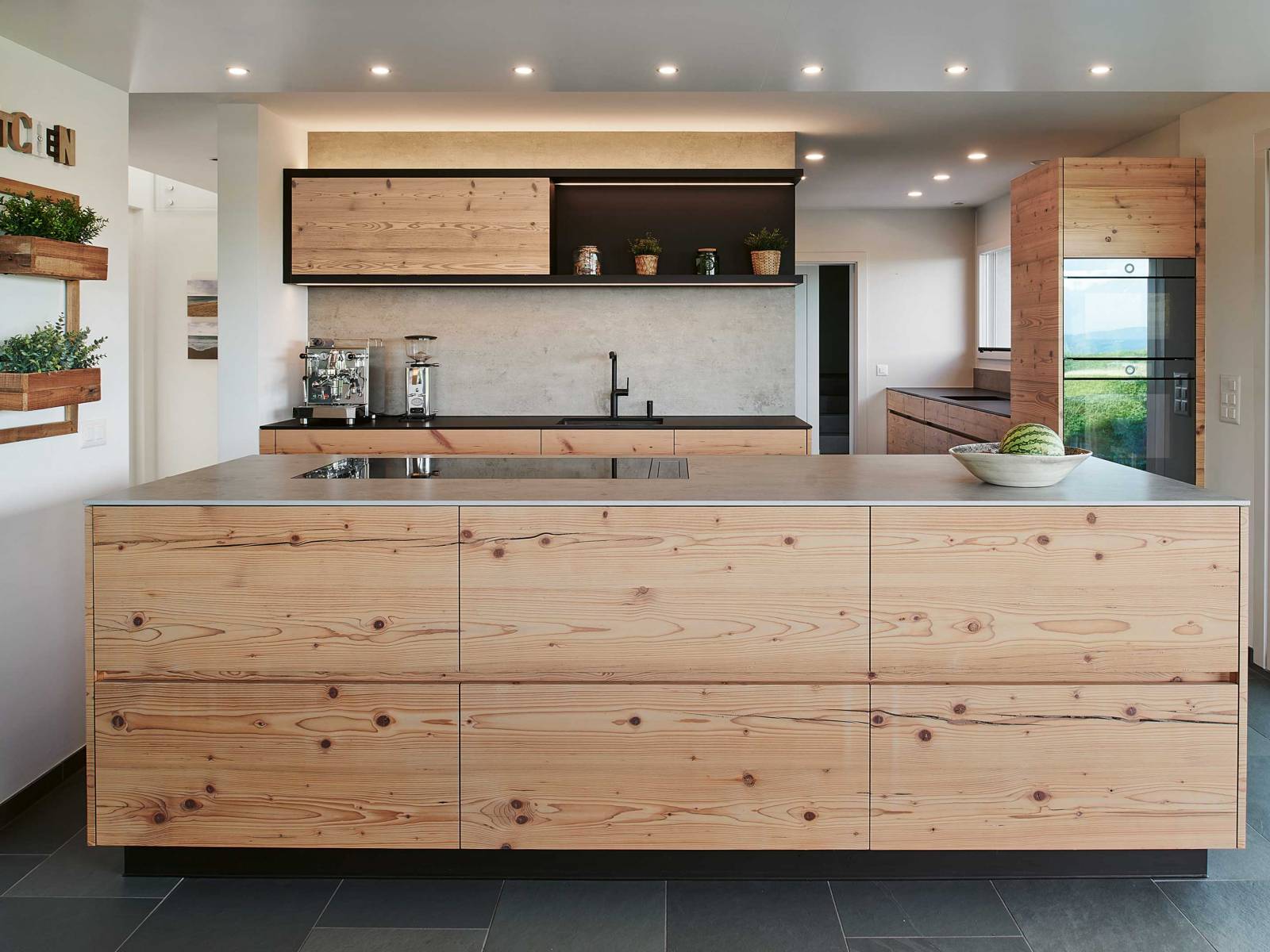 Eine Küche mit Charakter ist bei diesem Umbauprojekt entstanden, was nicht zuletzt auf die Materialwahl zurückzuführen ist. Denn für die Fronten wurde hier Altholz aus Fichte gewählt, das sich die Bauherrschaft vor Ort beim Küchenbauer ausgesucht hat, kombiniert mit einer Hochschrankzeile in Schwarz und einer Abdeckung in Betonoptik. BRUNNER KÜCHEN.
