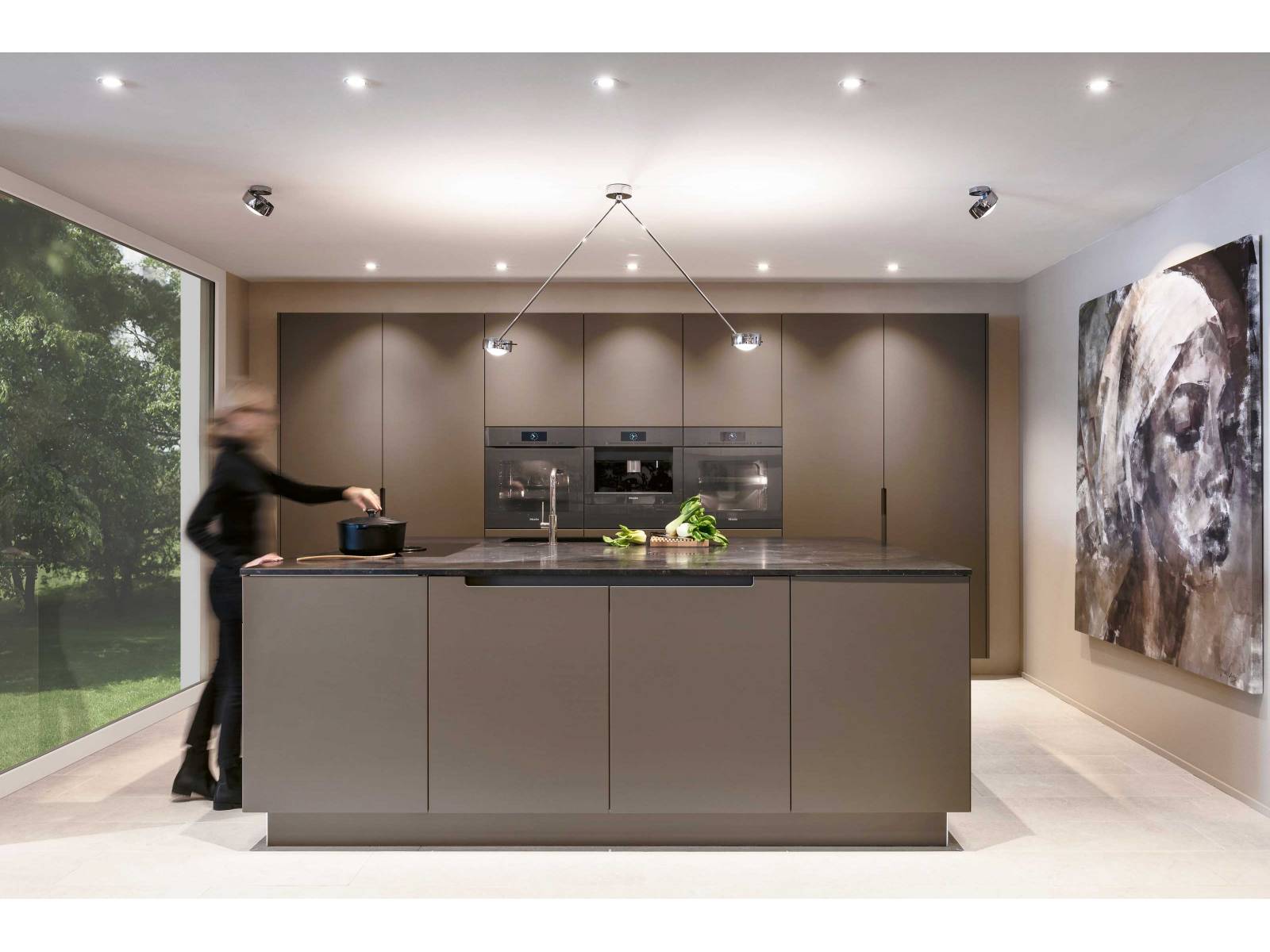 Symmetrie in vollendeter Form: Die auf Mass gefertigte Küche bespielt den Raum in seiner gesamten Breite, ist schlicht und sehr klar in ihrer Linienführung. Der dunkle Granit der Arbeitsfläche fügt sich nahtlos ins Gesamtbild aus schlammfarbigen Fronten und ebenfalls mittig angeordneten Einbaugeräten von Miele. ROLF SCHUBIGER.