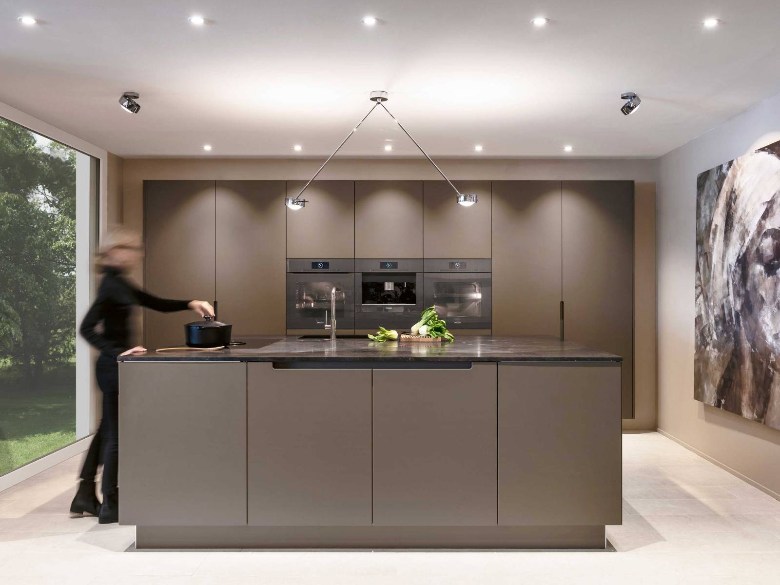 Symmetrie in vollendeter Form: Die auf Mass gefertigte Küche bespielt den Raum in seiner gesamten Breite, ist schlicht und sehr klar in ihrer Linienführung. Der dunkle Granit der Arbeitsfläche fügt sich nahtlos ins Gesamtbild aus schlammfarbigen Fronten und ebenfalls mittig angeordneten Einbaugeräten von Miele. ROLF SCHUBIGER.