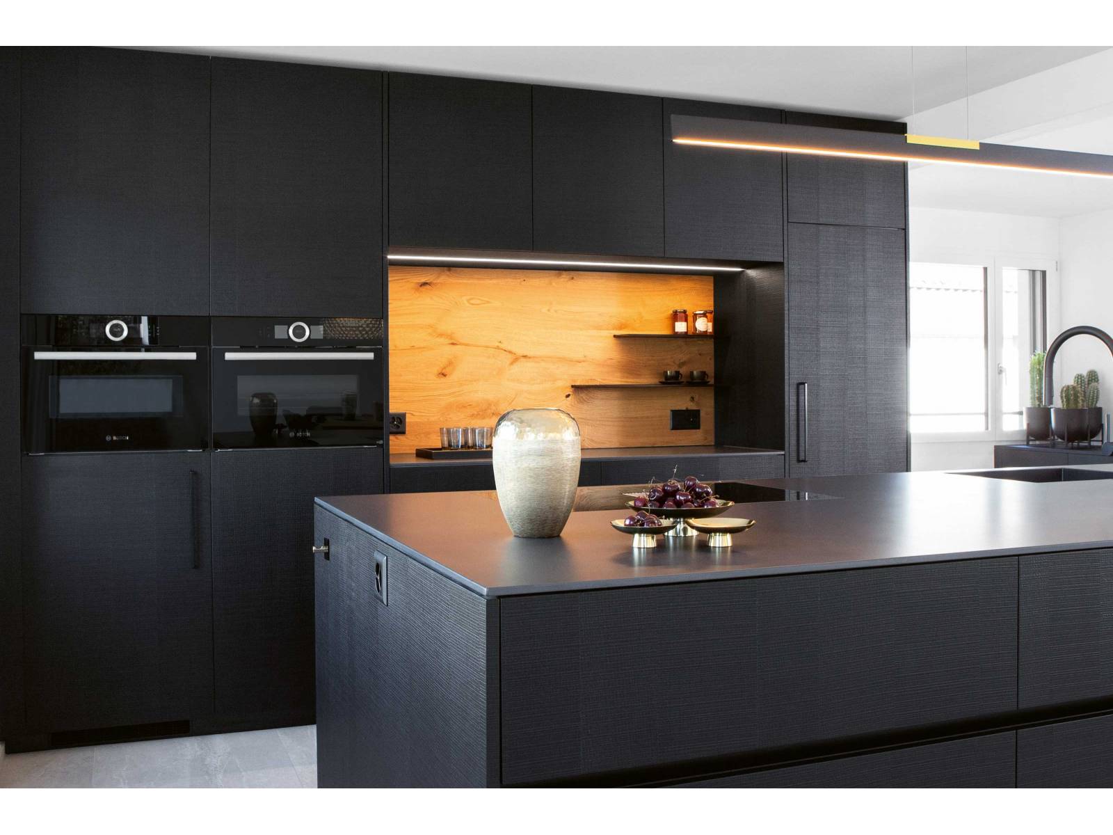 Das sägerohe, schwarz gebeizte und lackierte Eichenfurnier der Küchenfronten gibt jedem Zuhause eine ganz eigene Note und sorgt für ein besonderes haptisches Erlebnis. Während Küchenarmatur und Spülbecken ebenfalls in Schwarz gehalten sind, lockert die Nischenrückwand in heller Eiche das Ensemble auf. Foto: Klaus Andorfer. ELBAU.