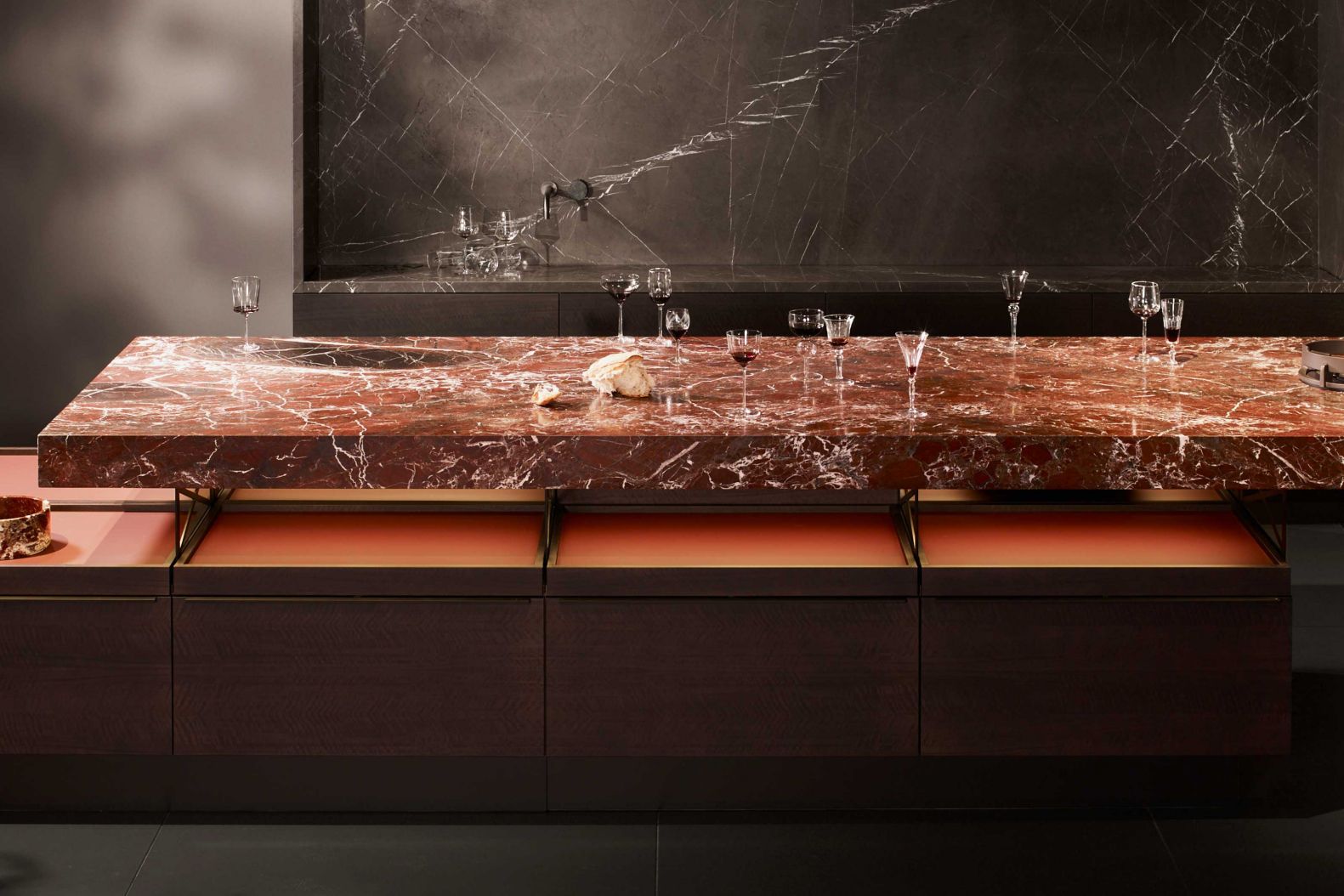 Rosso Lepanto heisst der imposante Naturstein aus Ligurien, dessen Schönheit in der Kollektion 2021 gekonnt zur Schau gestellt wird. Massive Blöcke sind unsichtbar zu einer langgestreckten Arbeitsplatte verbunden, die wie schwebend auf beleuchteten «+MODO»-Unterschränken in Eukalyptusholz ruht. Der exklusive Marmor zeichnet sich besonders durch seine feuerrote Färbung aus, die mit filigranen Adern in Schwarz und Weiss durchzogen ist. Poggenpohl.