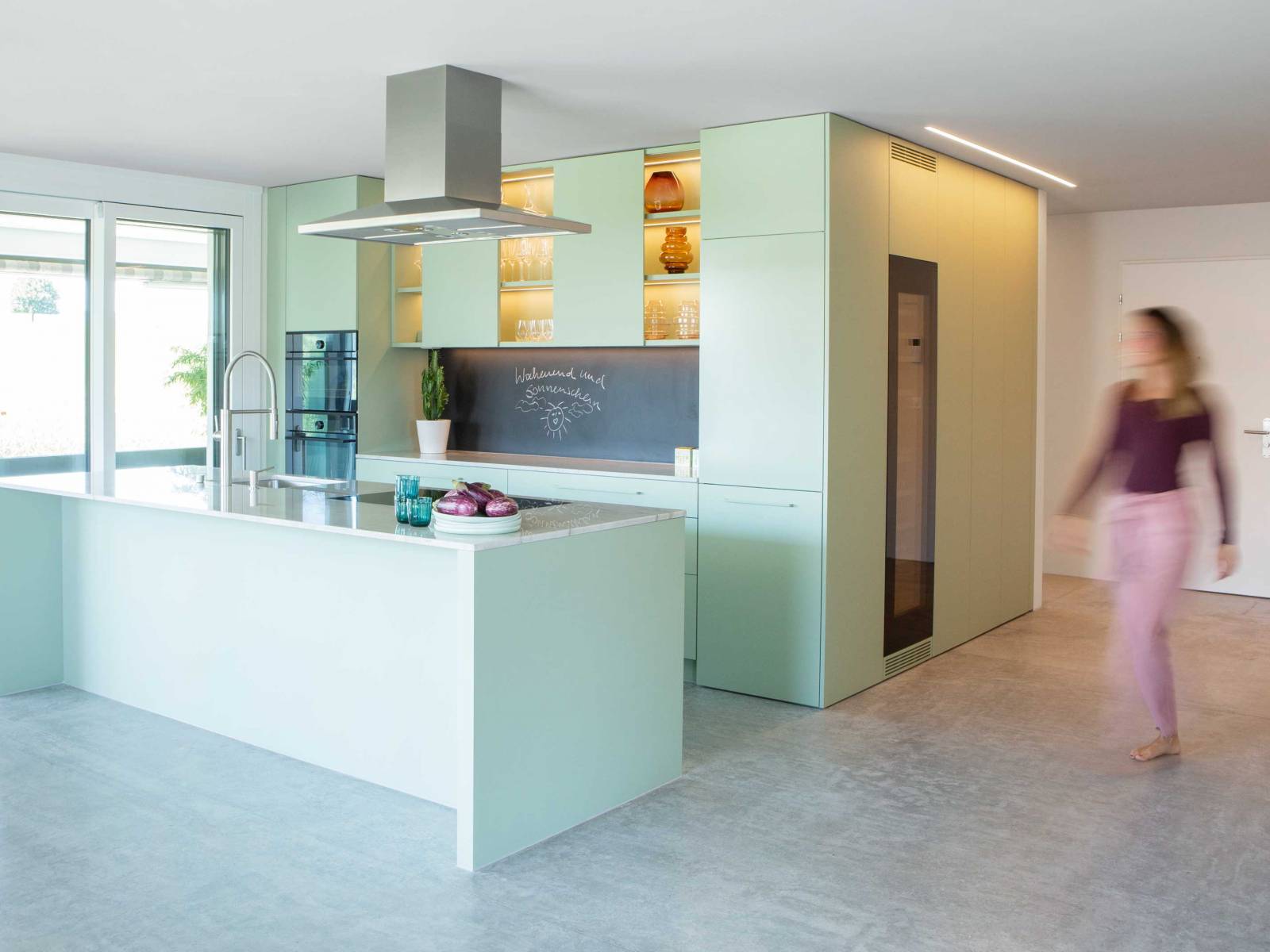 Diese auf Mass geplante Küche sorgt in Pistaziengrün für einen frischen Start in den Tag. Die Oberschränke spielen mit offenen und geschlossenen Elementen, was neben dem zarten Farbton zusätzlich für Leichtigkeit sorgt. Die dimmbare LED-Beleuchtung setzt schönes Geschirr gekonnt in Szene und sorgt für viel Atmosphäre. ELBAU.