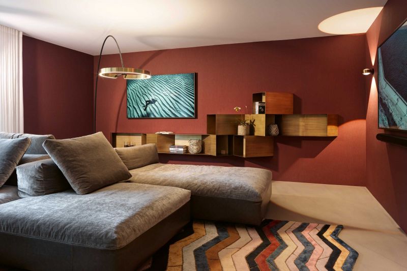 Vom Weiss zum Karminrot: Die Tapete im Wohnzimmer trägt den klangvollen Namen «Les unis flamant le rouge castille» und ist von Arte. Für die perfekte Beleuchtung der gesamten Etage sorgt das Leuchtensystem von Occhio, das mit seiner Gestensteuerung vor allem den Herrn des Hauses erfreut. Das Sofa: «Monopoli» von Desirée / Gruppoeuromobil ist mit dem Textil «Opera» von Designers Guild bezogen. Der Teppich «Pietra» ist von Christian Lacroix und wie auch die Vorhangstoffe «Valloire oyster» für Designers Guild.