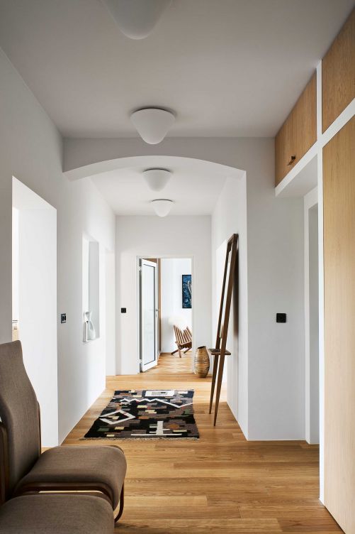 Der Bauherr verzichtete auf Fussleisten, um die Räume höher wirken zu lassen. Viele Brauntöne und unterschiedliche Hölzer sorgen im Flur für eine entspannte Atmosphäre. Der tschechische Designer Jan Bocan entwarf die Stühle 1972 für die tschechische Botschaft in Stockholm. Die polnischen Deckenleuchten aus Opalglas sorgen für sanftes Licht.