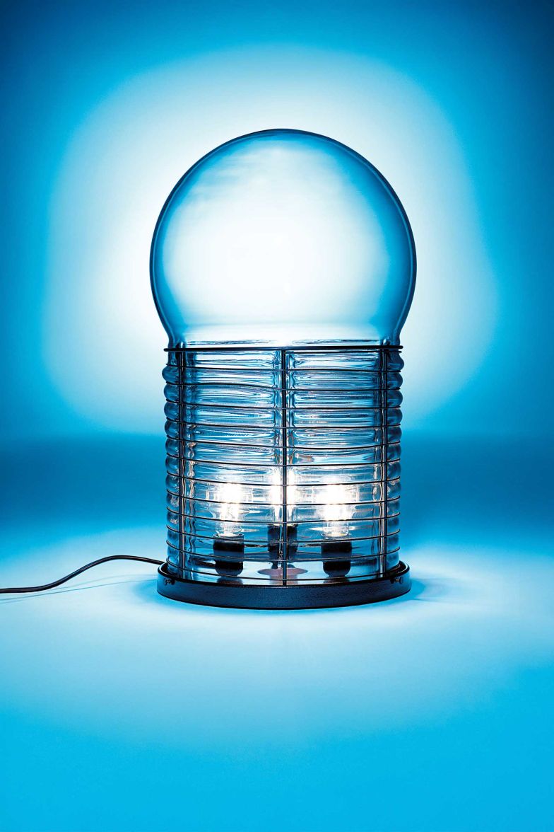 Die gläserne Tischleuchte «Alcinoo» von Gae Aulenti aus dem Jahr 1975 rückt in der «Masters’ Pieces»-Kollektion von Artemide wieder ins Rampenlicht. Sie ist ein Zeichen unvergänglicher Formkultur, in der technisches Können und poetische Aura zusammenfinden. Mund­ge­blasenes Glas, getragen von einer zarten Metallstruktur, erinnert an eine überdimensionierte Glühbirne und zeichnet eine unverkennbare Silhouette. Foto Ferrari. artemide.com