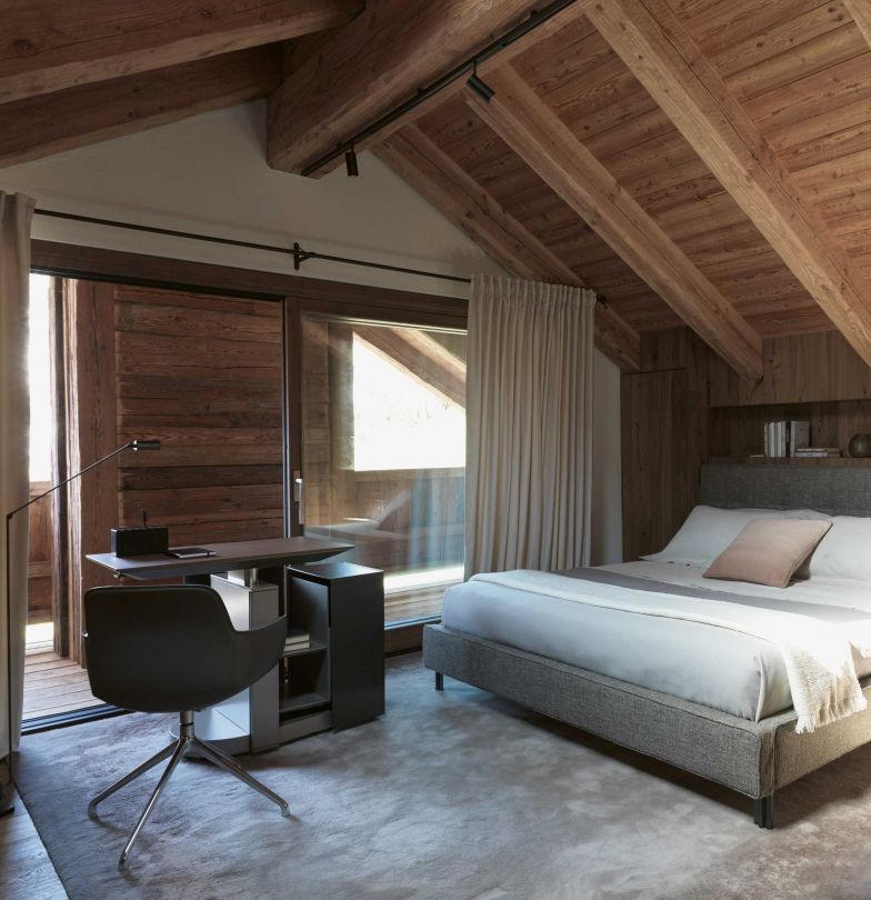 Die Innenräume der Chalets suchen die Verbindung zur Natur und fangen, wo es möglich ist, das stattliche Bergpanorama ein. Für eine besonders elegante Atmosphäre sorgen hochwertige Möbel wie das Bett «Anton» von Vincent Van Duysen für Molteni & C/Dada oder der Schreibtisch «Touch Down Unit» von Studio Klaas für Unifor.